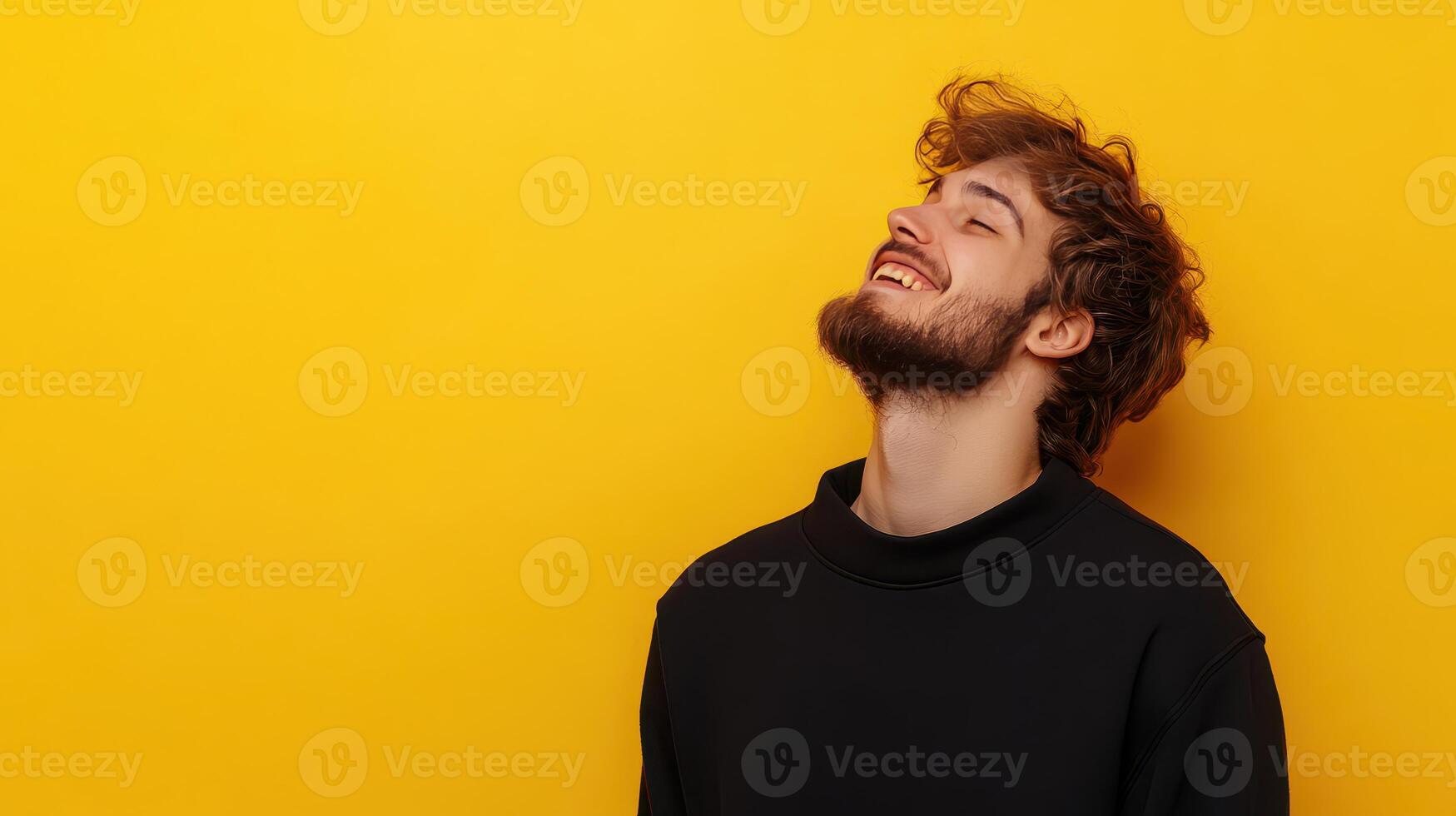 Young man smiling against vibrant yellow background in casual black attire during a joyful moment photo