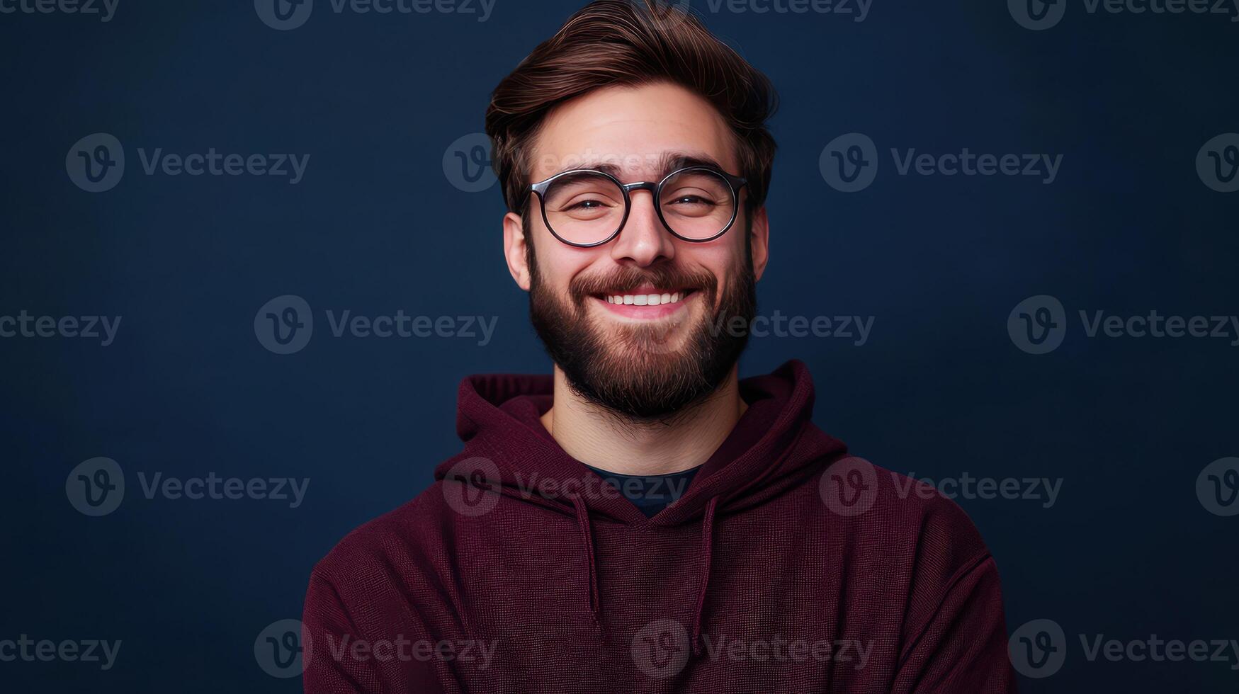 Young man with beard and glasses smiling warmly against a dark blue background photo