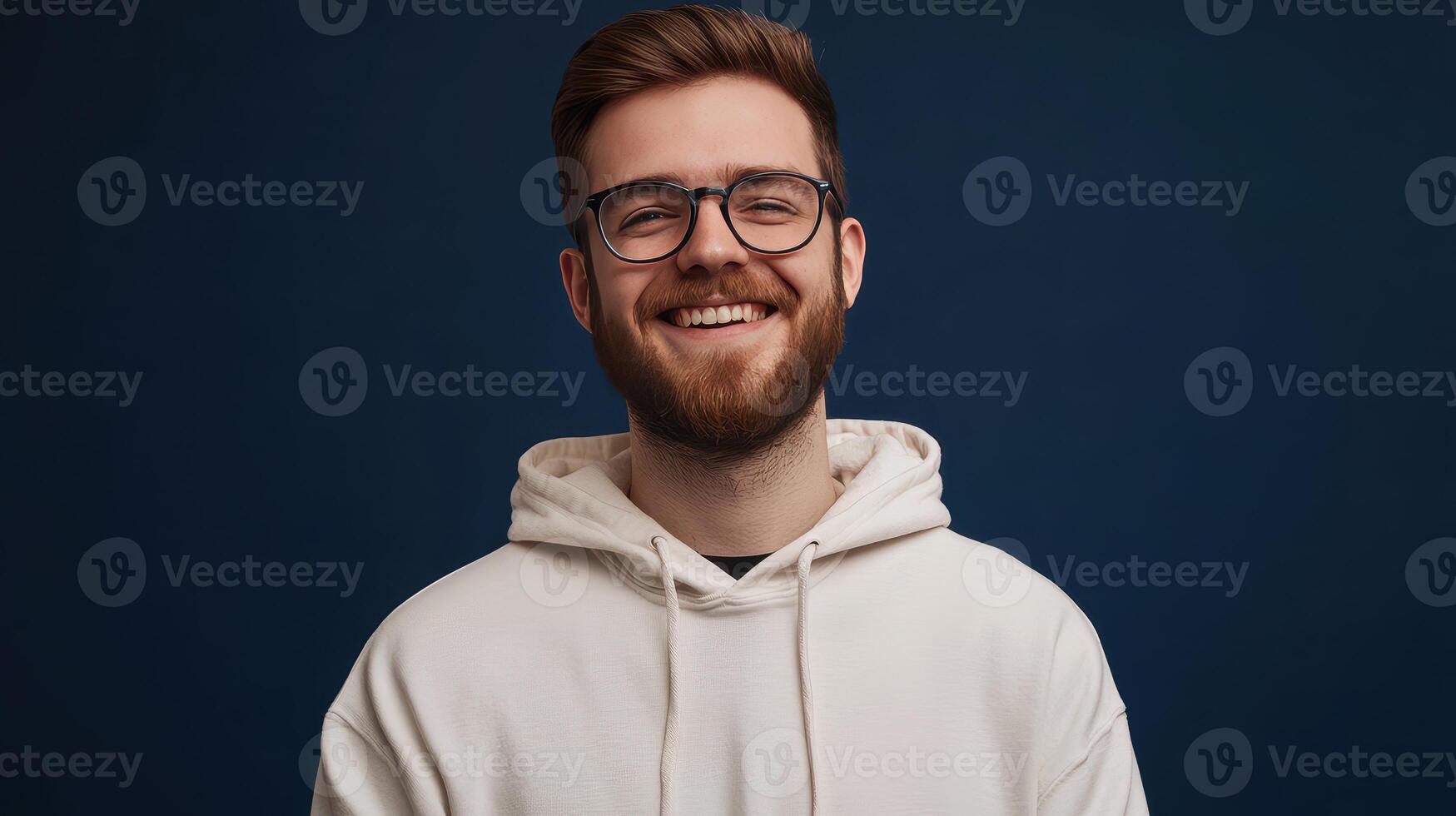 Young man with glasses smiling warmly against a dark blue backdrop while wearing a white hoodie photo