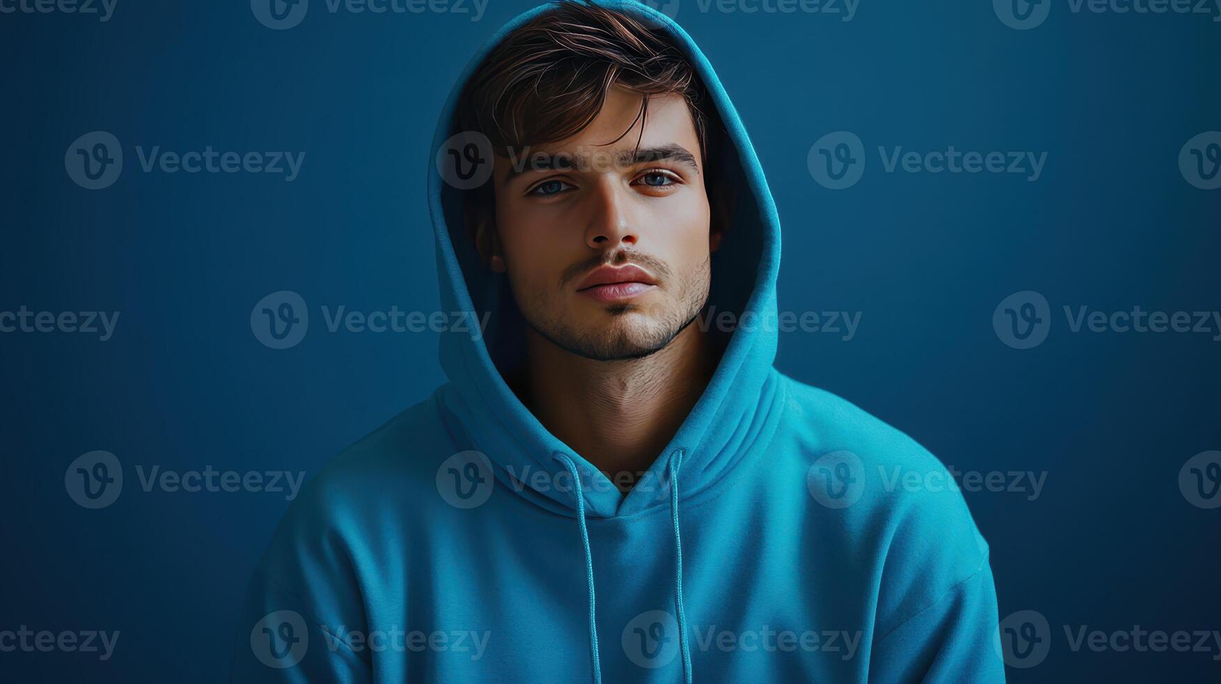 Young man in a turquoise hoodie poses against a dark blue background indoors photo