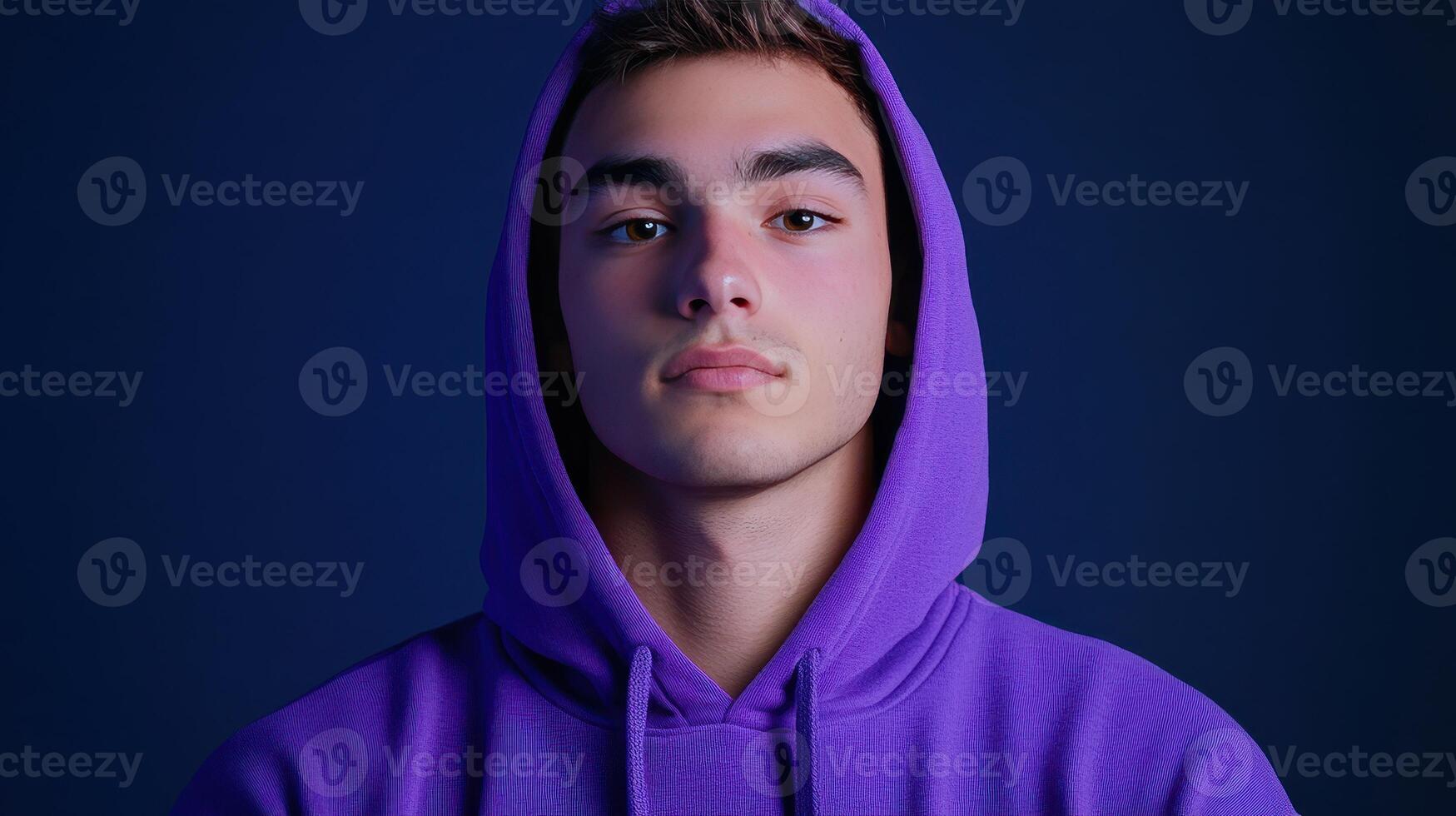 Young man in a purple hoodie against a dark background, showcasing a confident expression in a contemporary portrait taken indoors photo