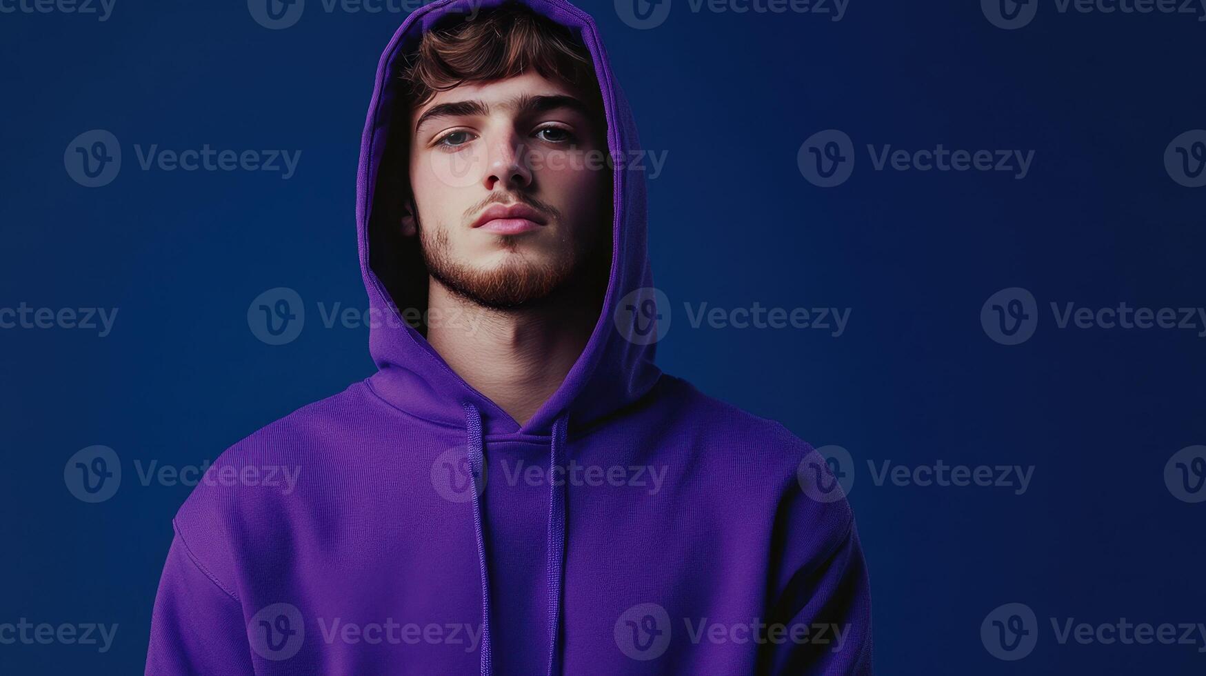Young man in a purple hoodie against a blue background, posing confidently with a serious expression photo