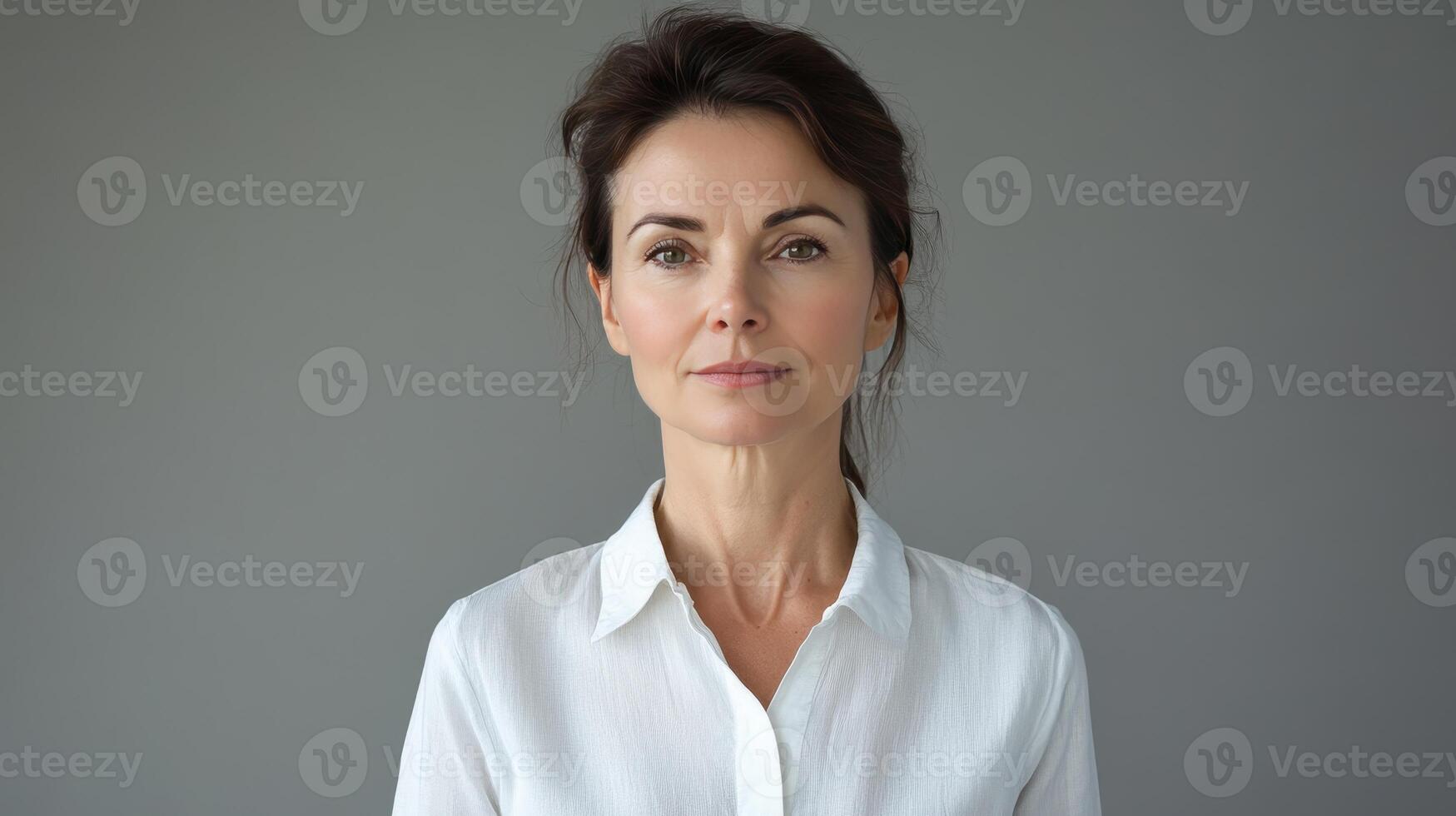 A woman in a white shirt poses against a gray backdrop in a calm and composed manner during a studio session photo