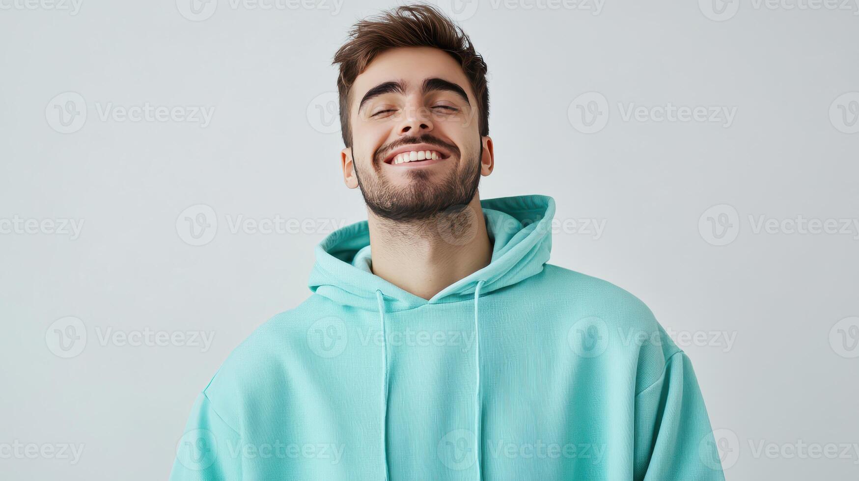 Smiling young man wearing a turquoise hoodie against a light background during cheerful indoor moment photo
