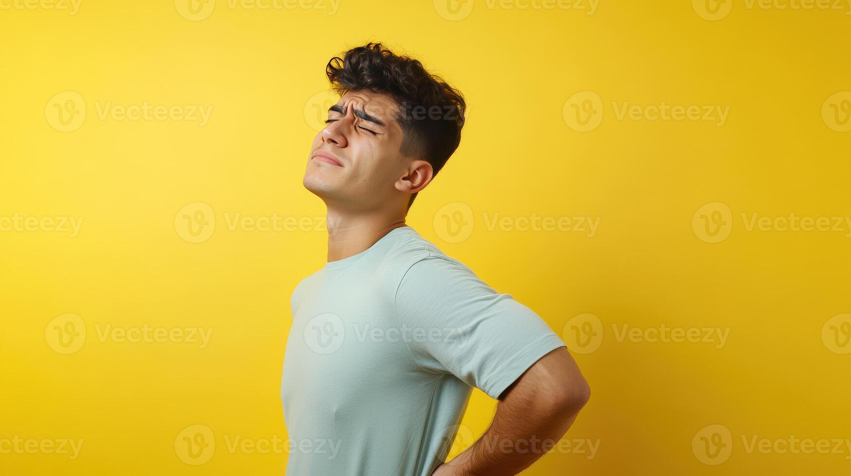 Man experiencing back pain while standing against a bright yellow background in a casual setting photo