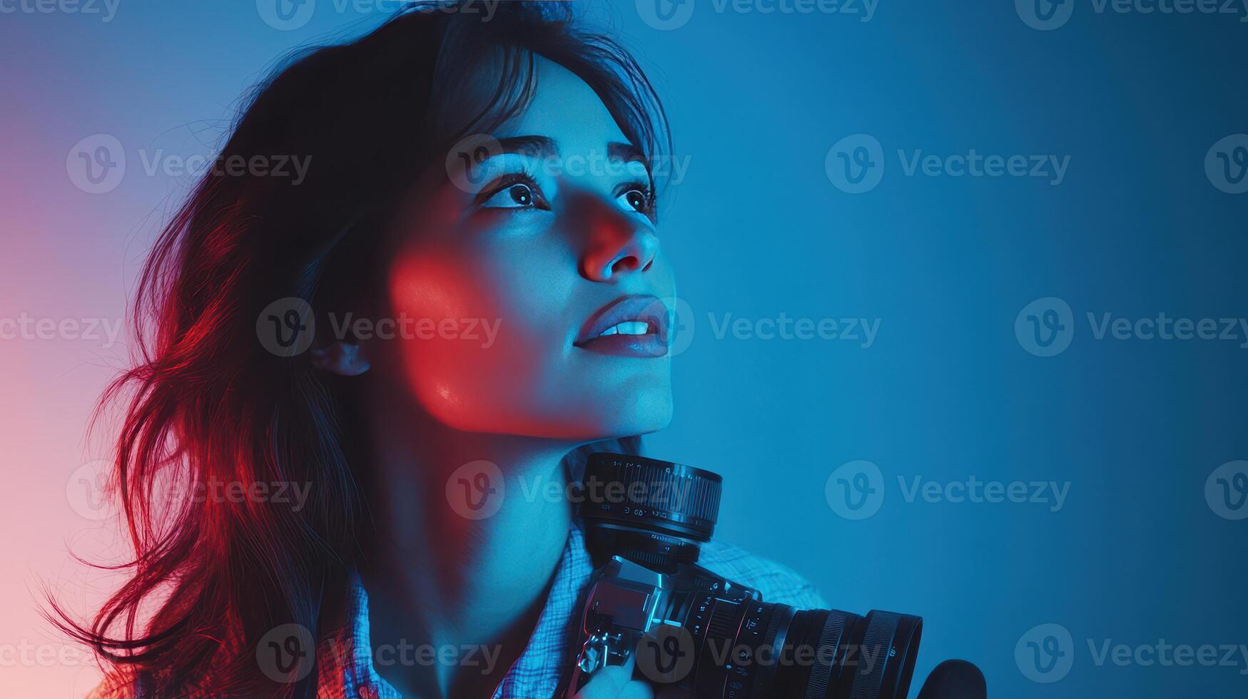 Young woman holds a vintage camera while gazing upward against a colorful blue and red backdrop photo