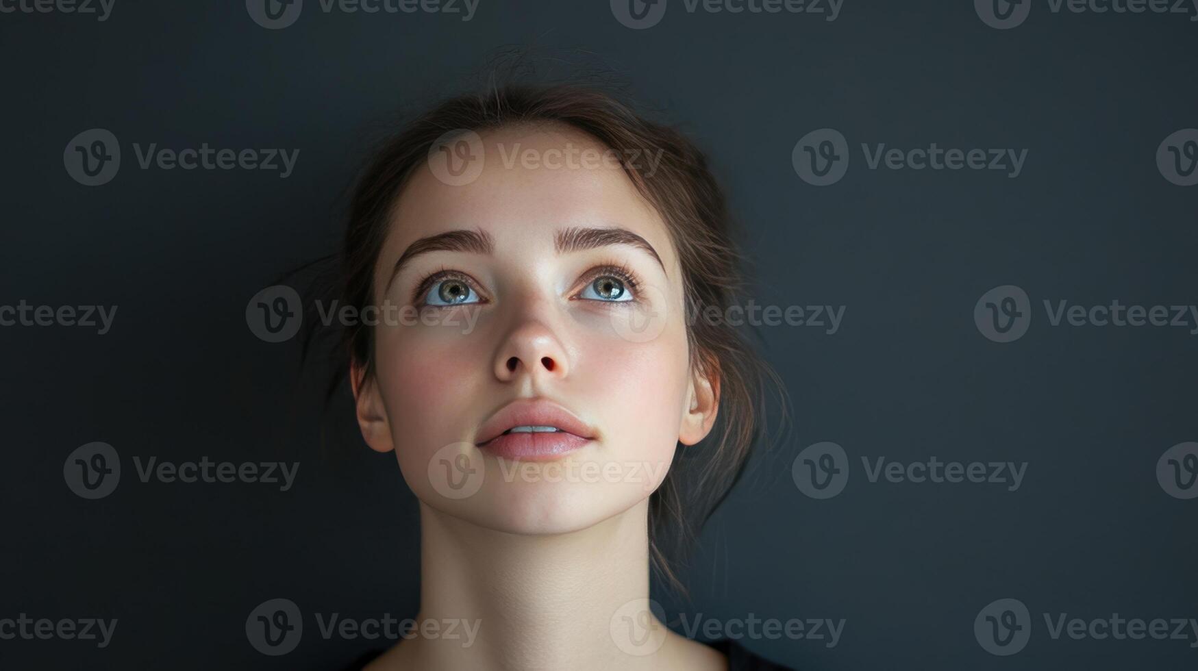 Young woman gazing upwards, with soft lighting and a neutral gray background, capturing a moment of contemplation and serenity indoors photo