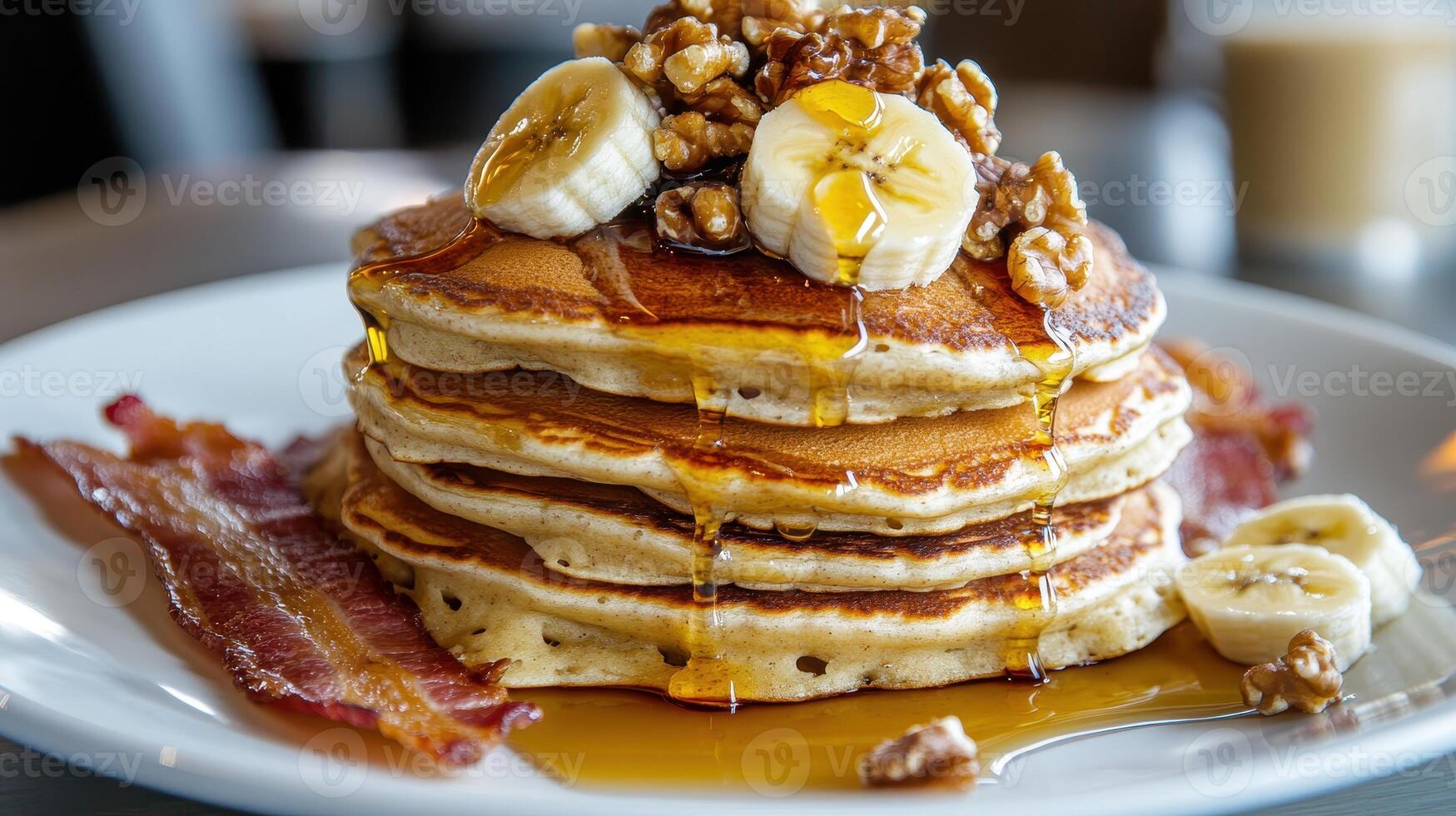 Delicious stack of pancakes topped with bananas, walnuts, and syrup served with crispy bacon photo