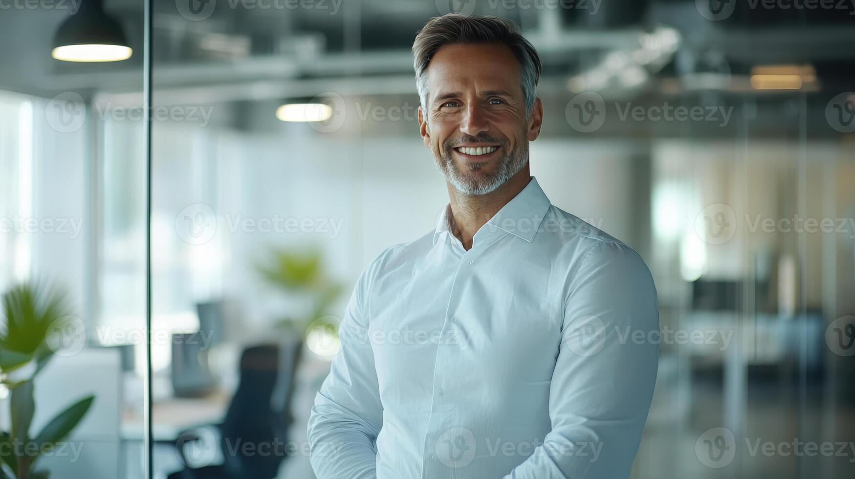 Professional man smiling in a modern office setting during daytime, with plants and workstations in the background photo