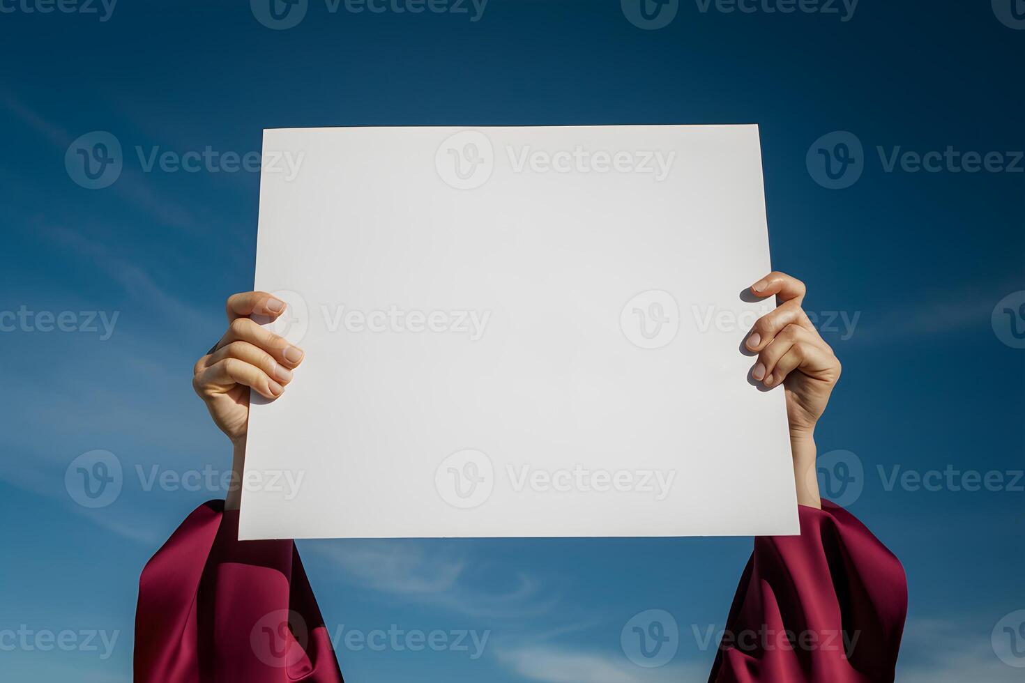 Hands holding white square against blue sky, maroon garment contrast photo