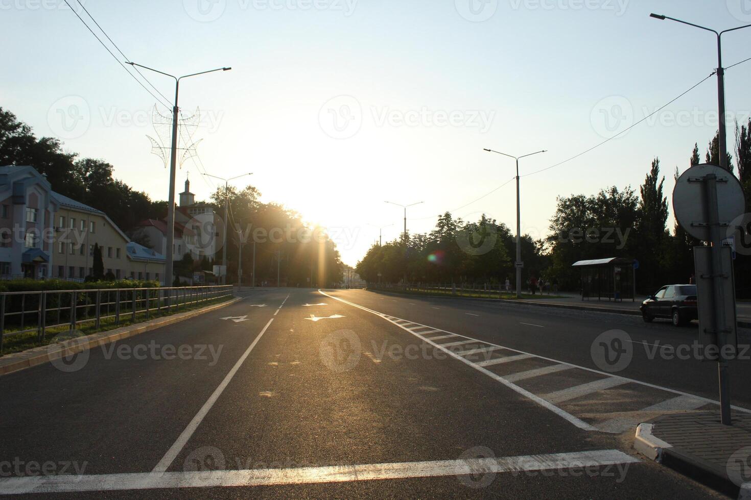A straight road without people and cars with the sun on top. A road through abandoned cities. Empty streets without people photo