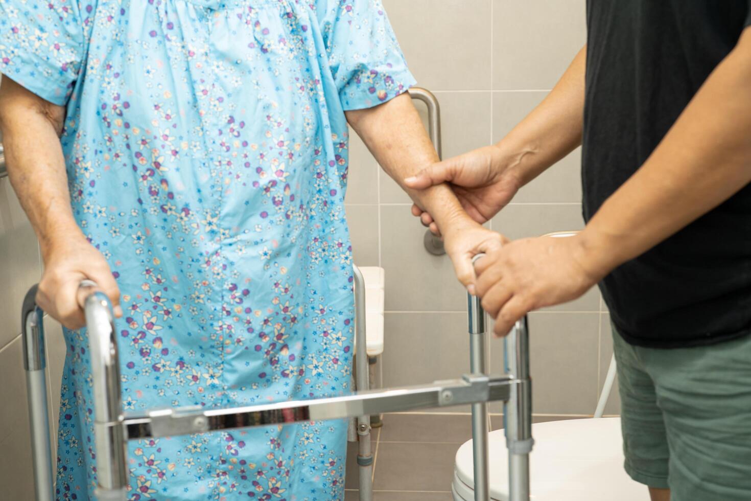 Caregiver help Asian elderly woman patient use walker and toilet bathroom handle security. photo