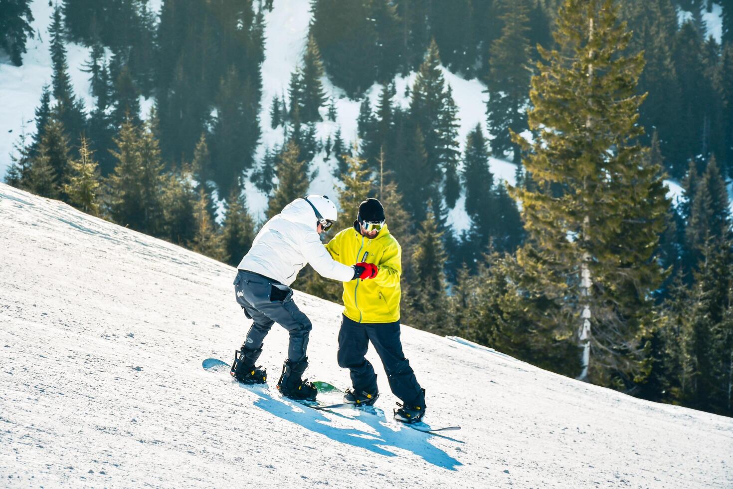 Goderdzi, Georgia - 13 th january, 2023 - male hipster instructor hold hands show how to snowboard keep balance beginner snowboarder downhill on white slope in ski resort. Lessons learn to ski photo