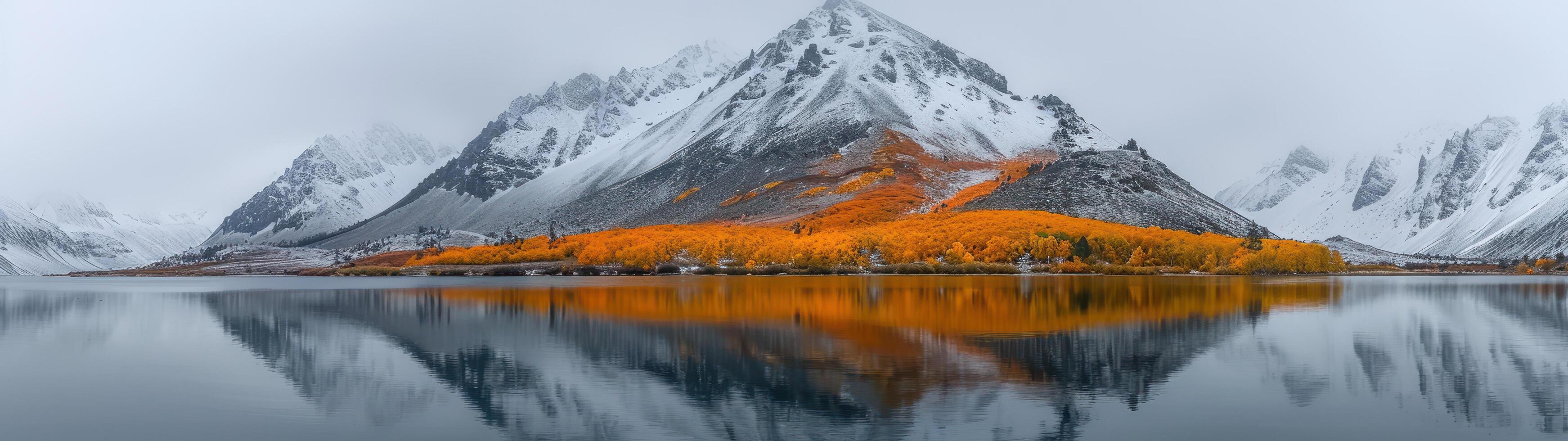 A panoramic view captures a snowy mountain with orange trees at its base, reflected in a lake beneath an overcast sky photo