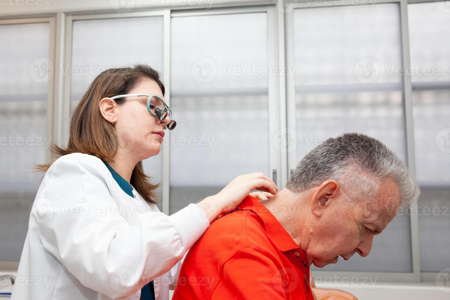 Dermatologist making a routine checkup on a senior male patient using a binocular loupe. photo