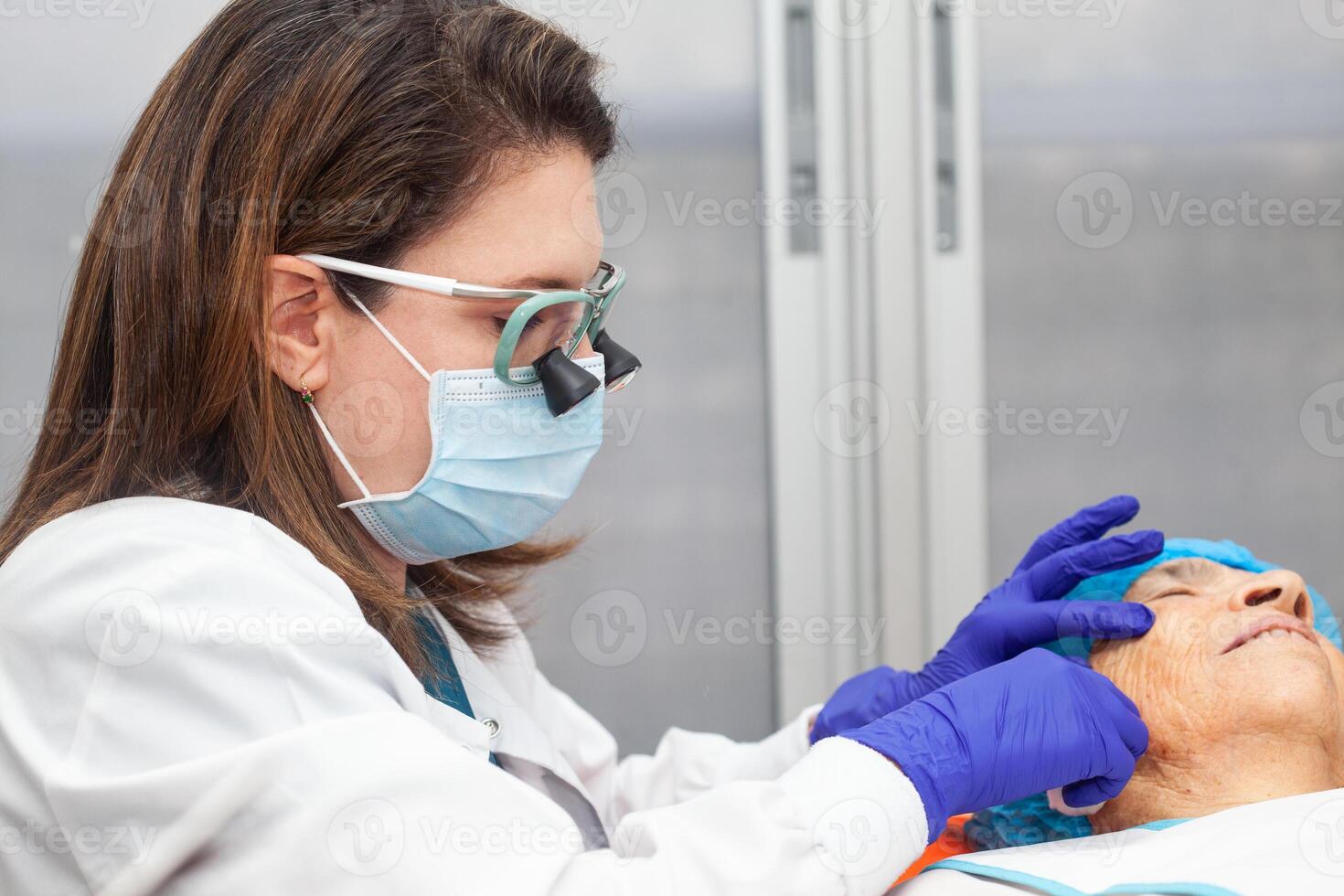 Dermatologist carrying out a skin biopsy on the face of a senior adult patient photo
