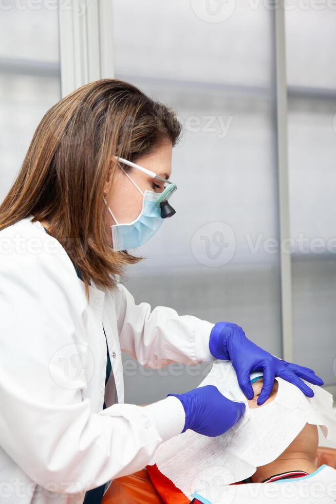 Skin lesion removal procedure. Dermatologist carrying out a removal of benign skin lesion on the face of a young male patient. Local anesthesia photo