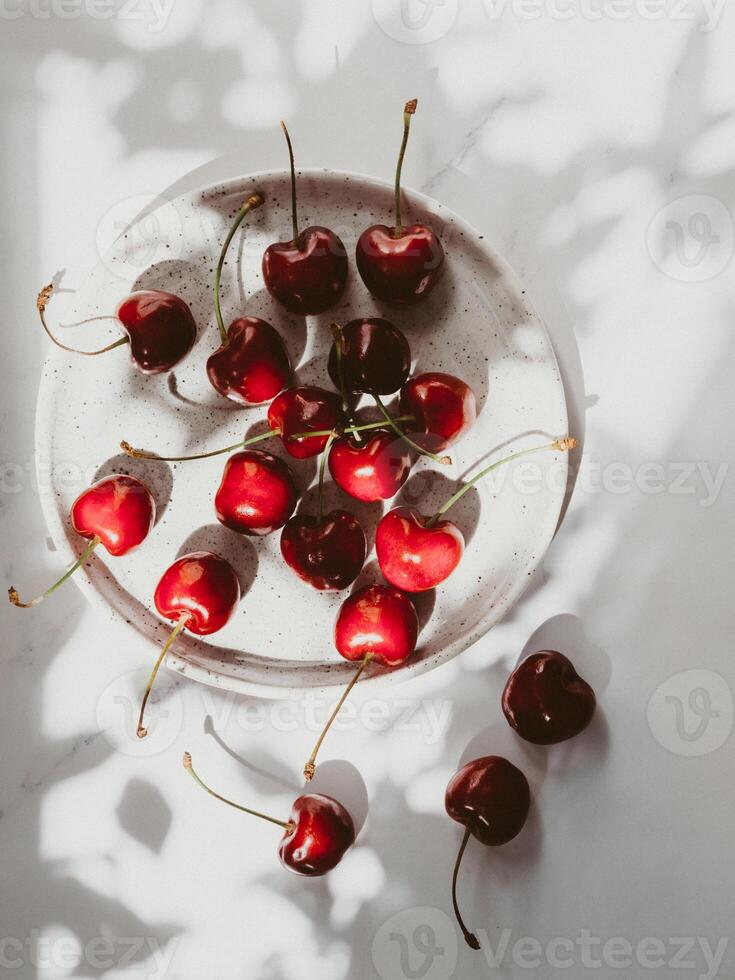 Plate of cherries on bright background in sunlight and the shadows of the leaves of the tree photo