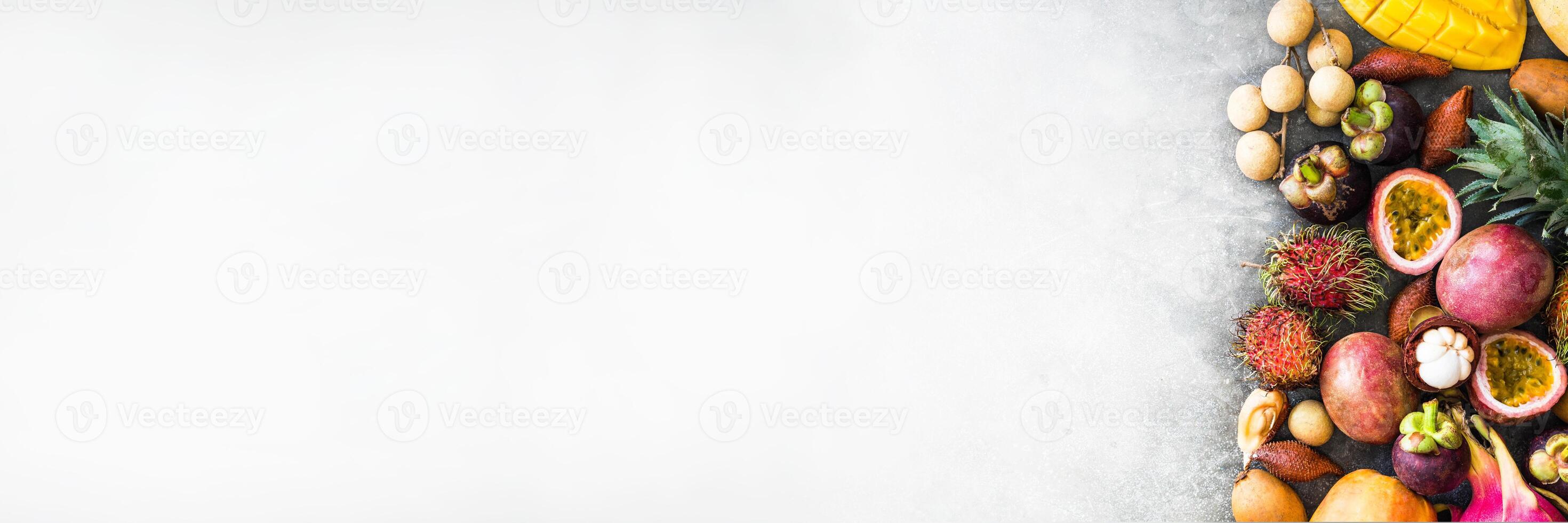 Various fresh Thai fruits - rambutan, mango, mangosteen, longan, papaya, dragon fruit, sapodilla, passion fruit, salak, pineapple on a wooden tray and a gray background. Top view. Copy space photo