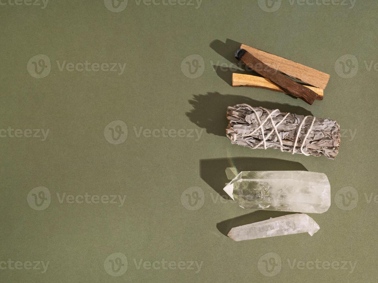 Items for spiritual cleansing - sage bundle, palo santo incense sticks and quartz crystal on green background. photo