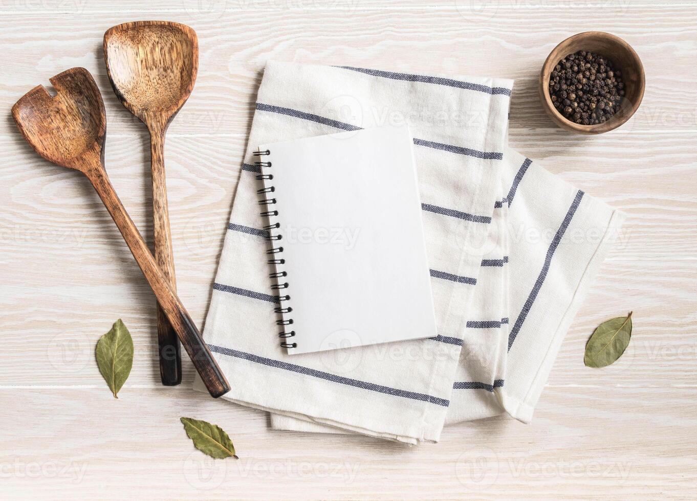 Minimal white kitchen background with blank notebook for text, cotton napkin, various spices and wood appliances. photo