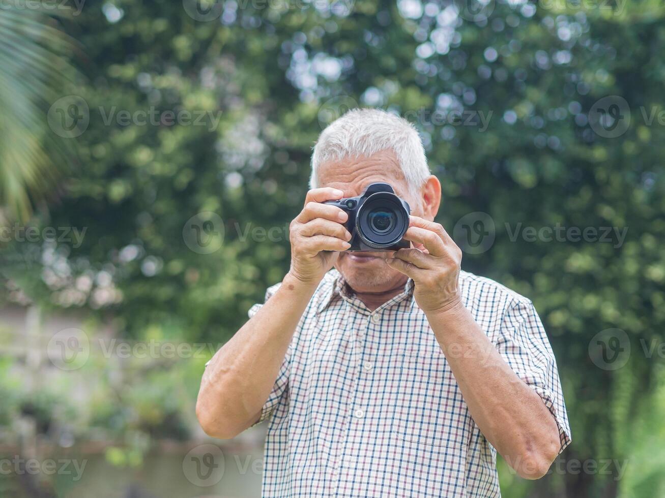 Happy senior man taking photographs with a digital camera while standing outdoors. Aged people photographer and relaxation concept photo
