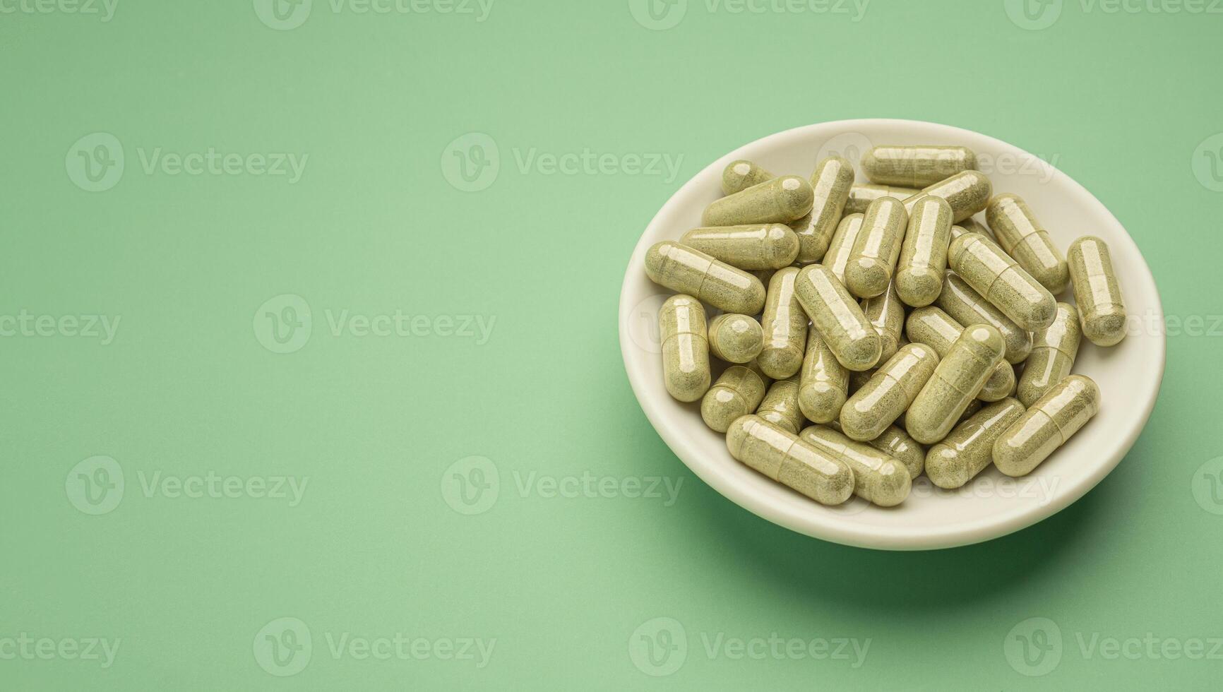 Flat lay of Andrographis capsules in a dish isolated on a green background. Space for text. Herbal, medicine, and healthcare concept photo