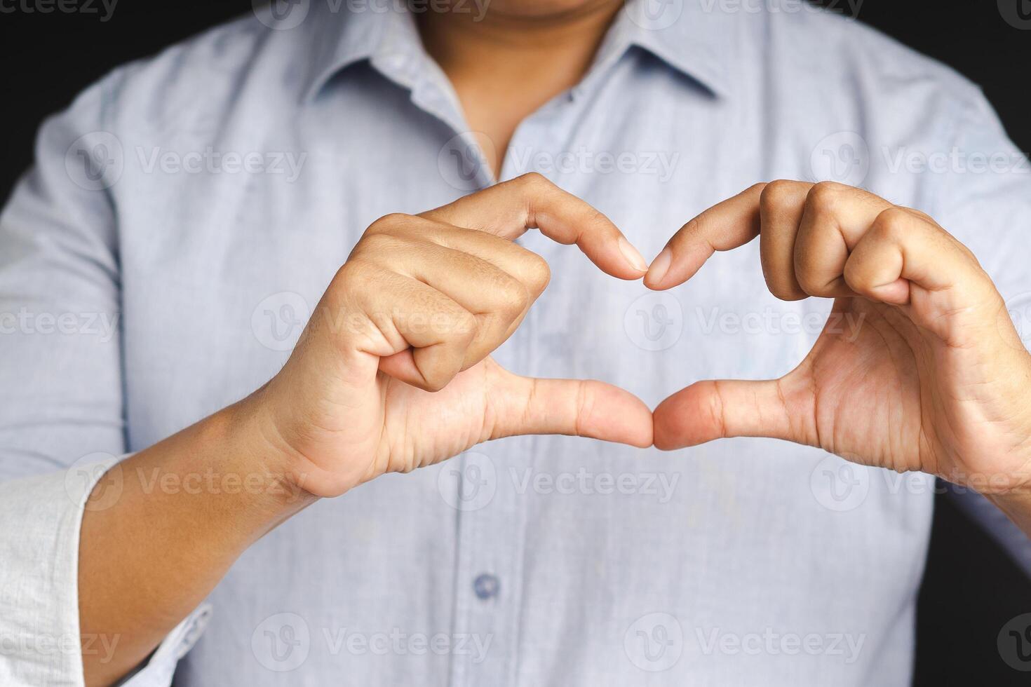 Man making heart figure love sign with fingers while standing in the studio. Positive human emotions, feelings, body language, attitude. Valentine's day. photo