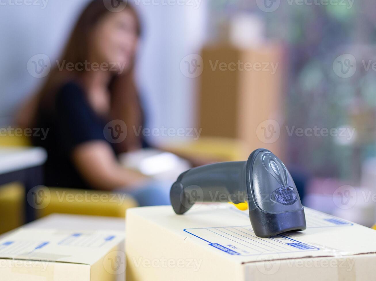Close-up of parcel boxes and barcode reader with a young couple sitting on a chair in the office. Blurred background. Concept of business and e-commerce photo