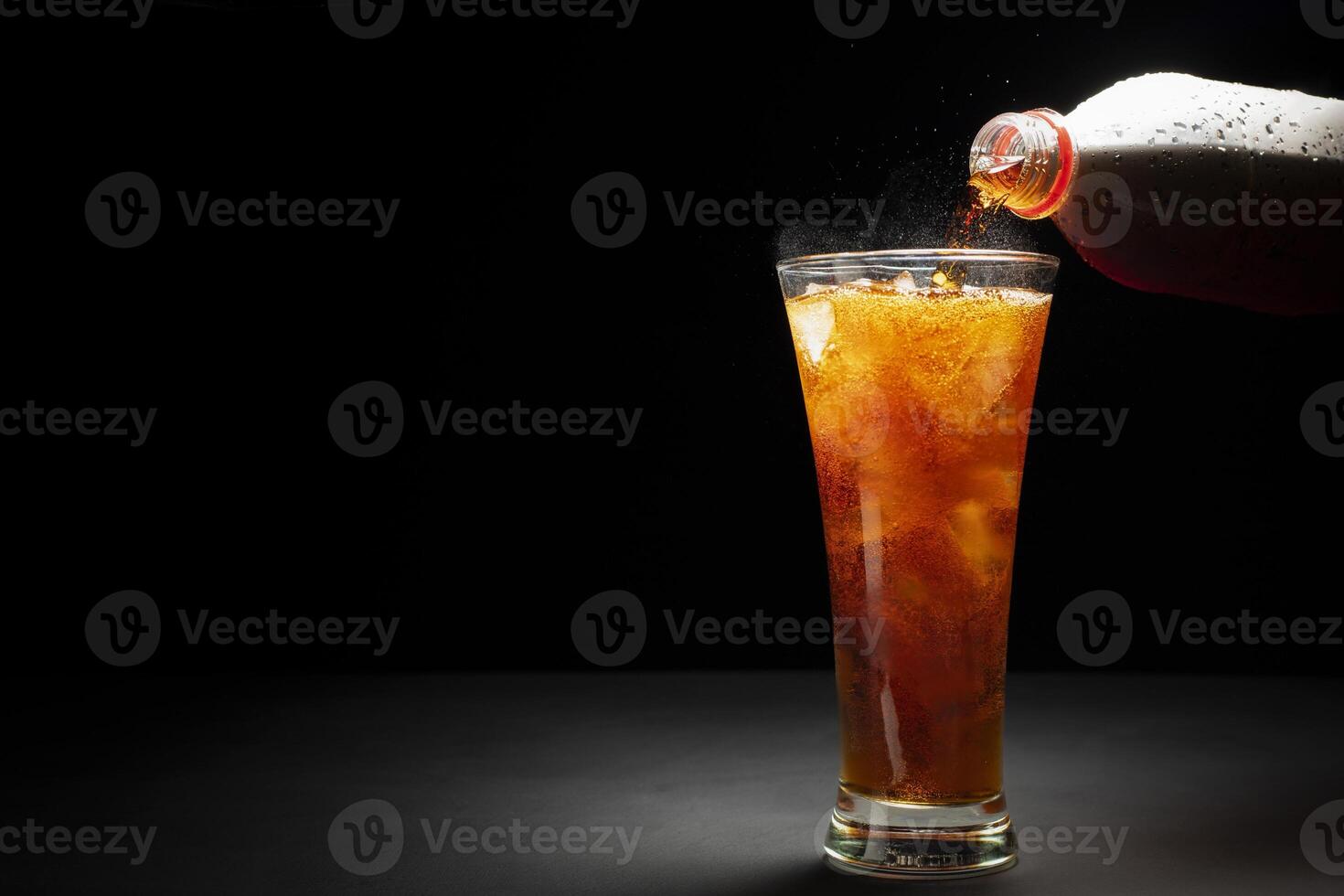 Black soda. Close-up of pouring soda with ice in a glass. Placed on a black and dark background. photo