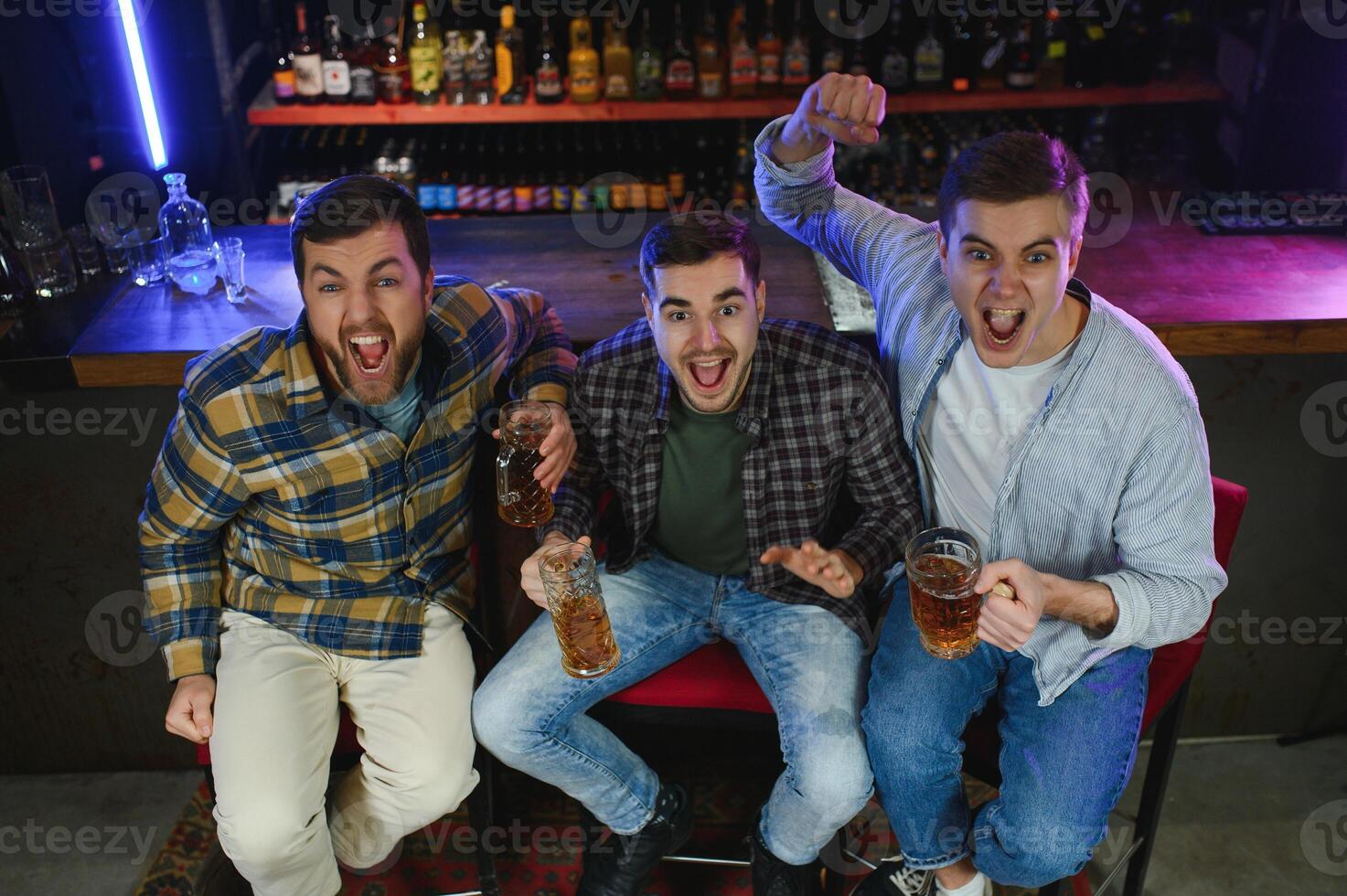 Soccer fans at the bar. Happy football fans cheering at bar and drinking beer while bartender serving beer at the background photo