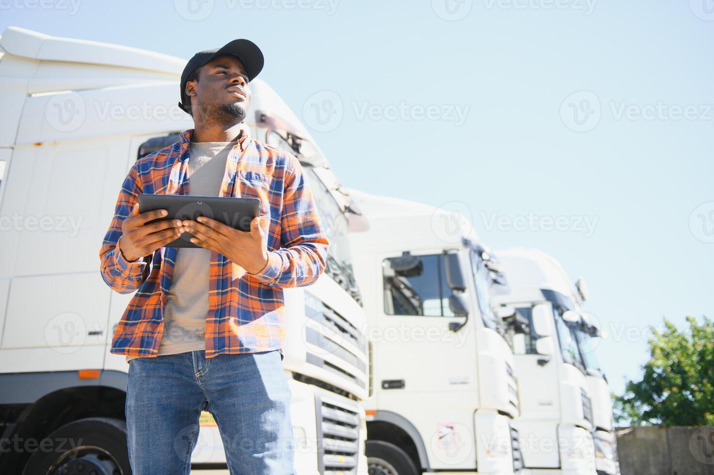 African American professional truck driver setting up navigation for destination. Checking his route on tablet computer and standing by long vehicle. Transportation service photo