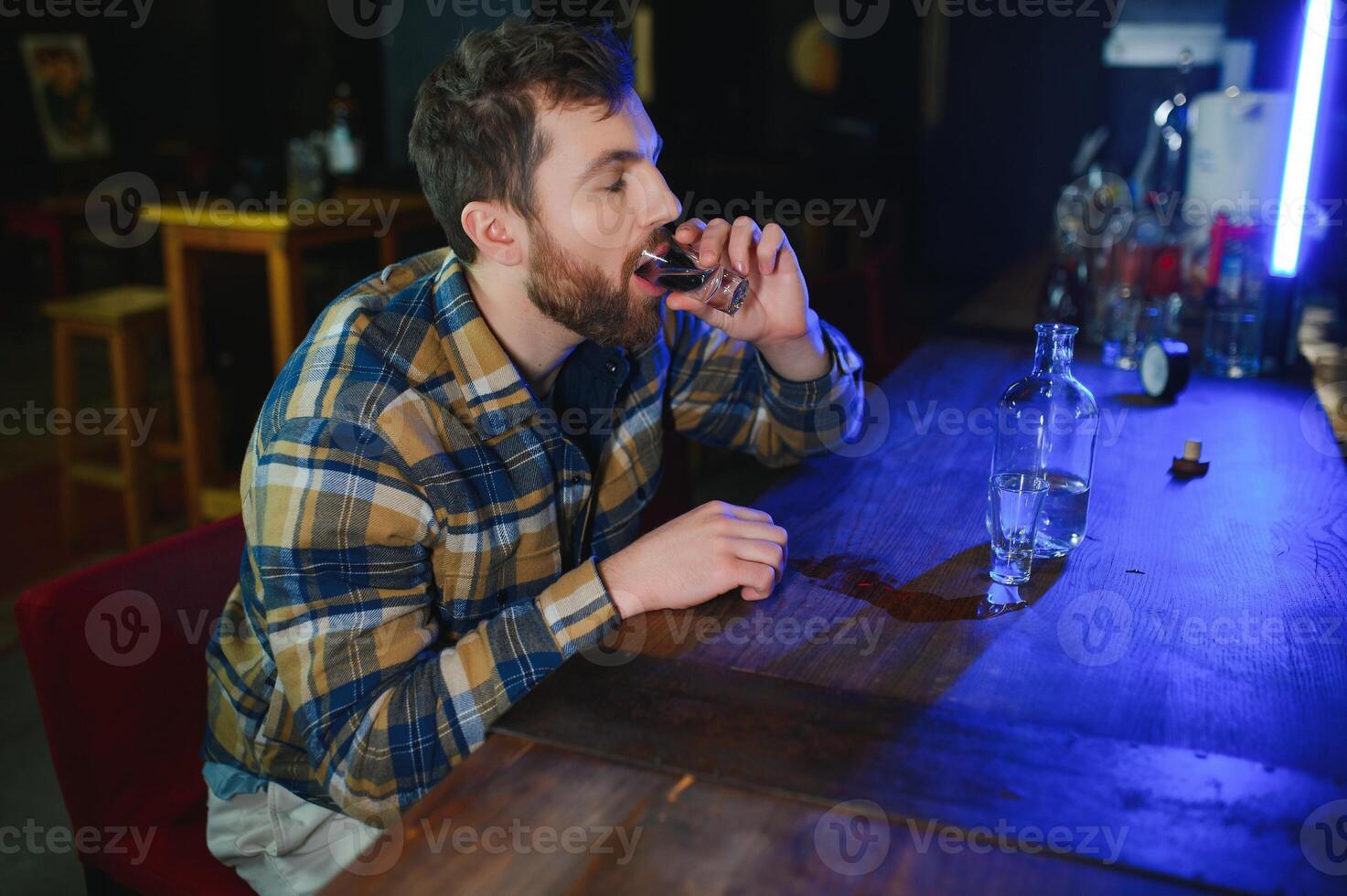Sad young man sitting at bar counter in pub. Upset man drinks alcohol because of problems at work. photo