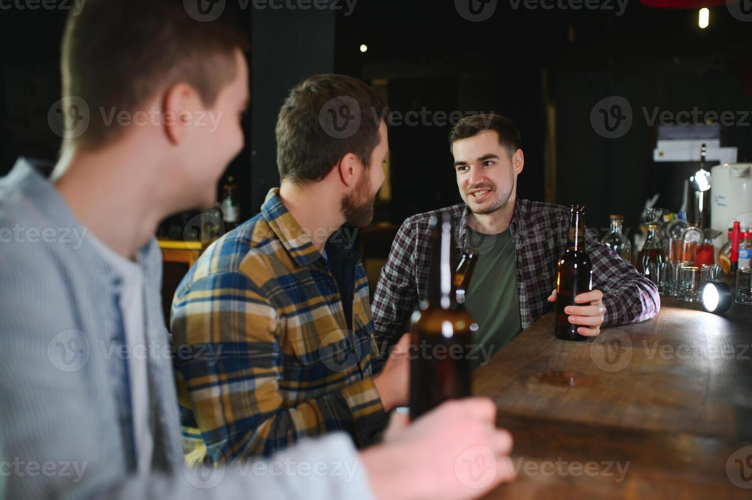 Young men in casual clothes are talking, laughing and drinking while sitting at bar counter in pub photo