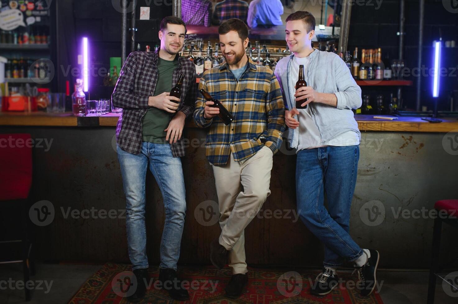 Friends having fun. Happy young men in casual wear drinking beer in pub. photo