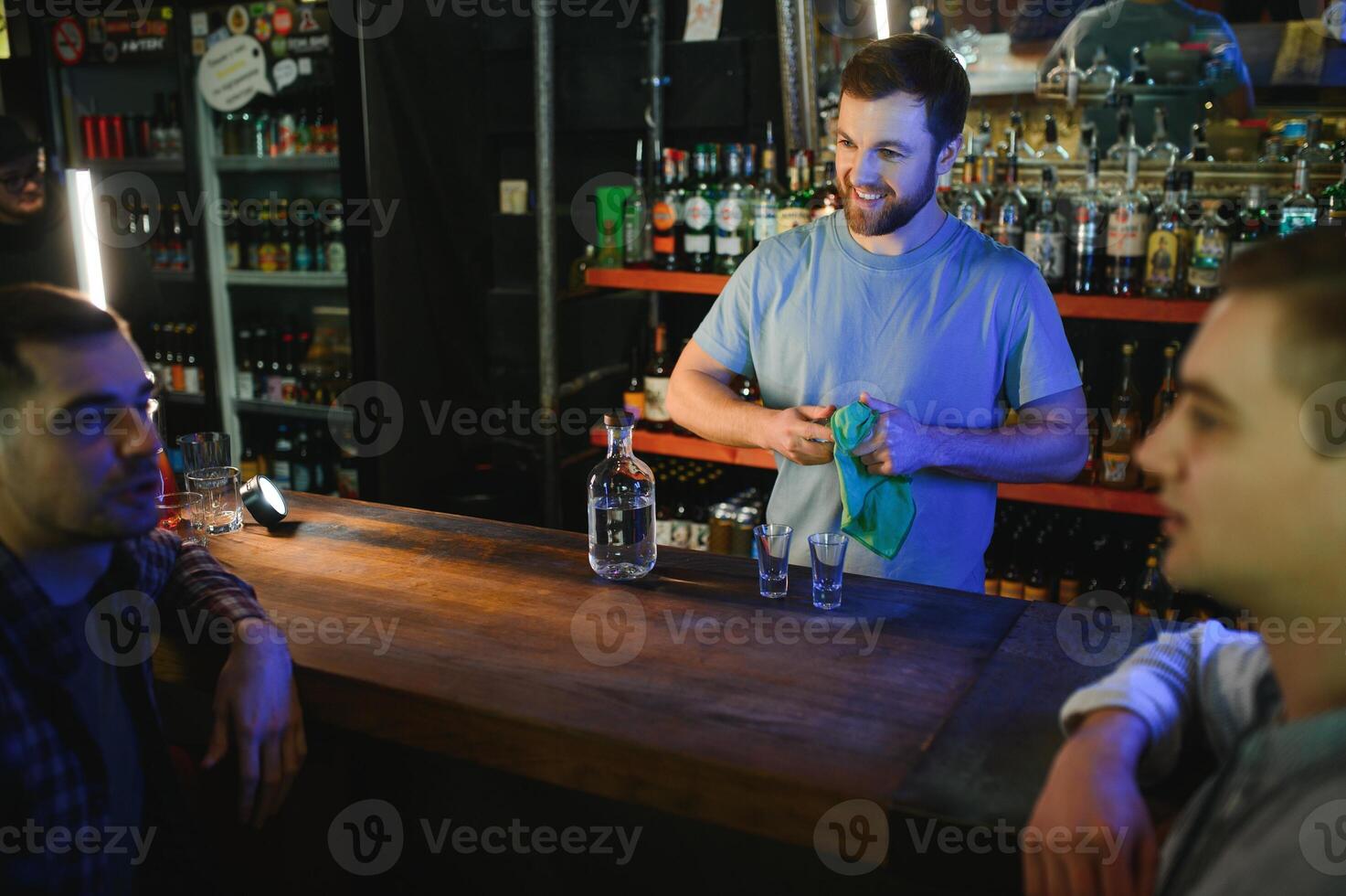 Attractive bartender is smiling and taking order of two men sitting at bar counter in pub photo