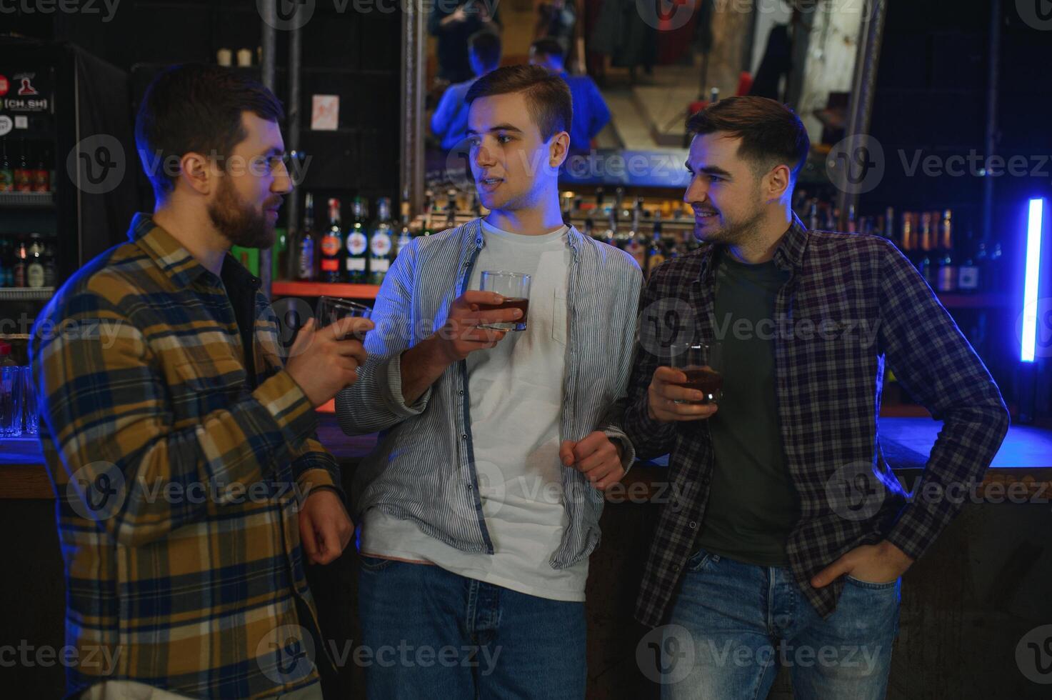 male friends spending time together in bar and having fun. Bearded men smiling, looking at each other and communicating. Men holding crystal glasses of whisky or scotch. photo