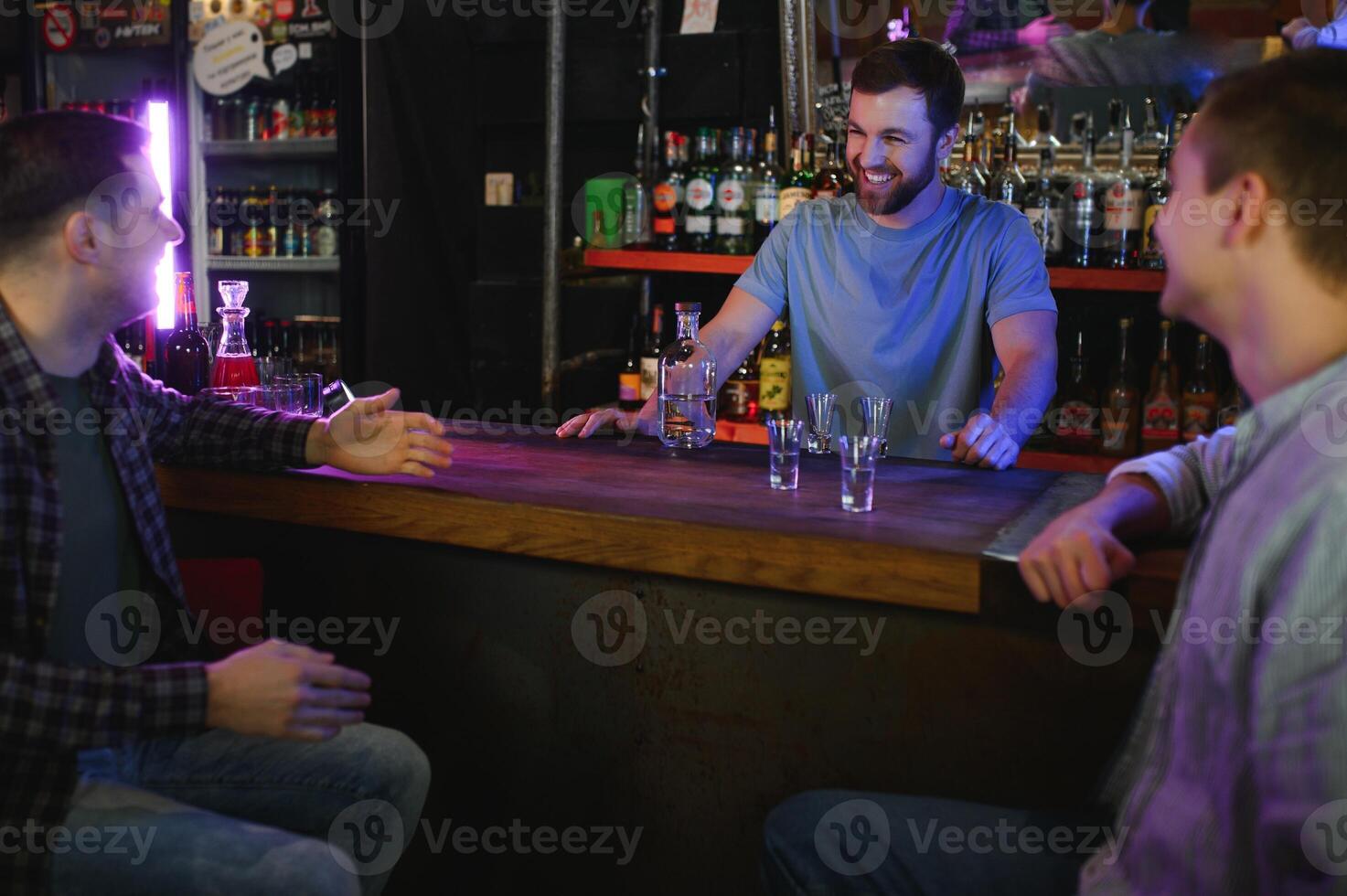 Attractive bartender is smiling and taking order of two men sitting at bar counter in pub photo