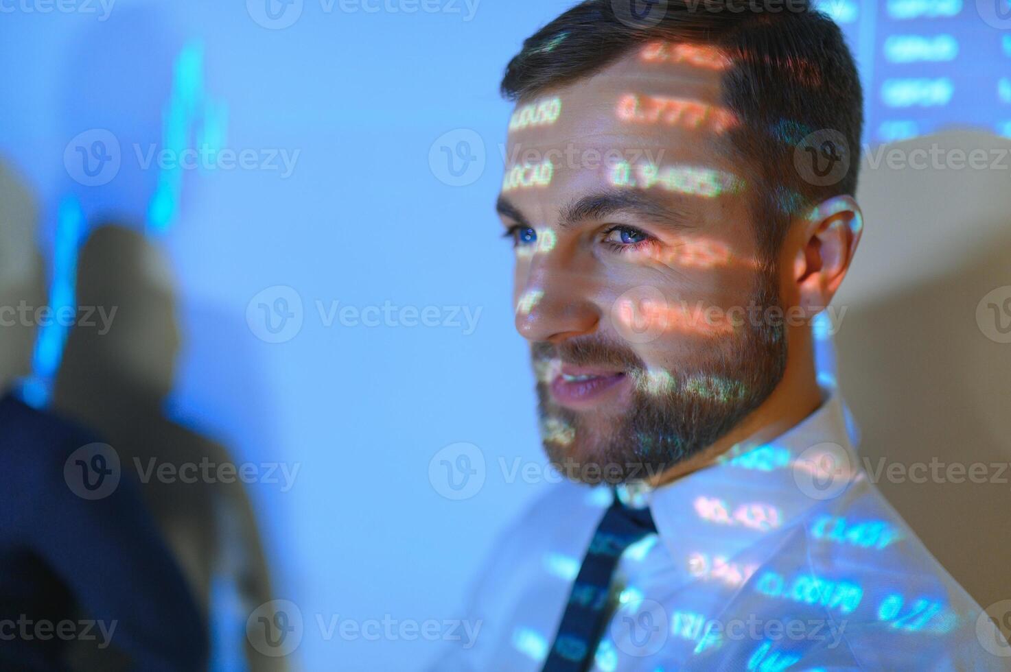 Stock Market Top Trader Looks at Projected Ticker Numbers and Graphs Running, Analysing Data to Make Best Sell. Behind Him Room Full of Screens and Statistics. photo