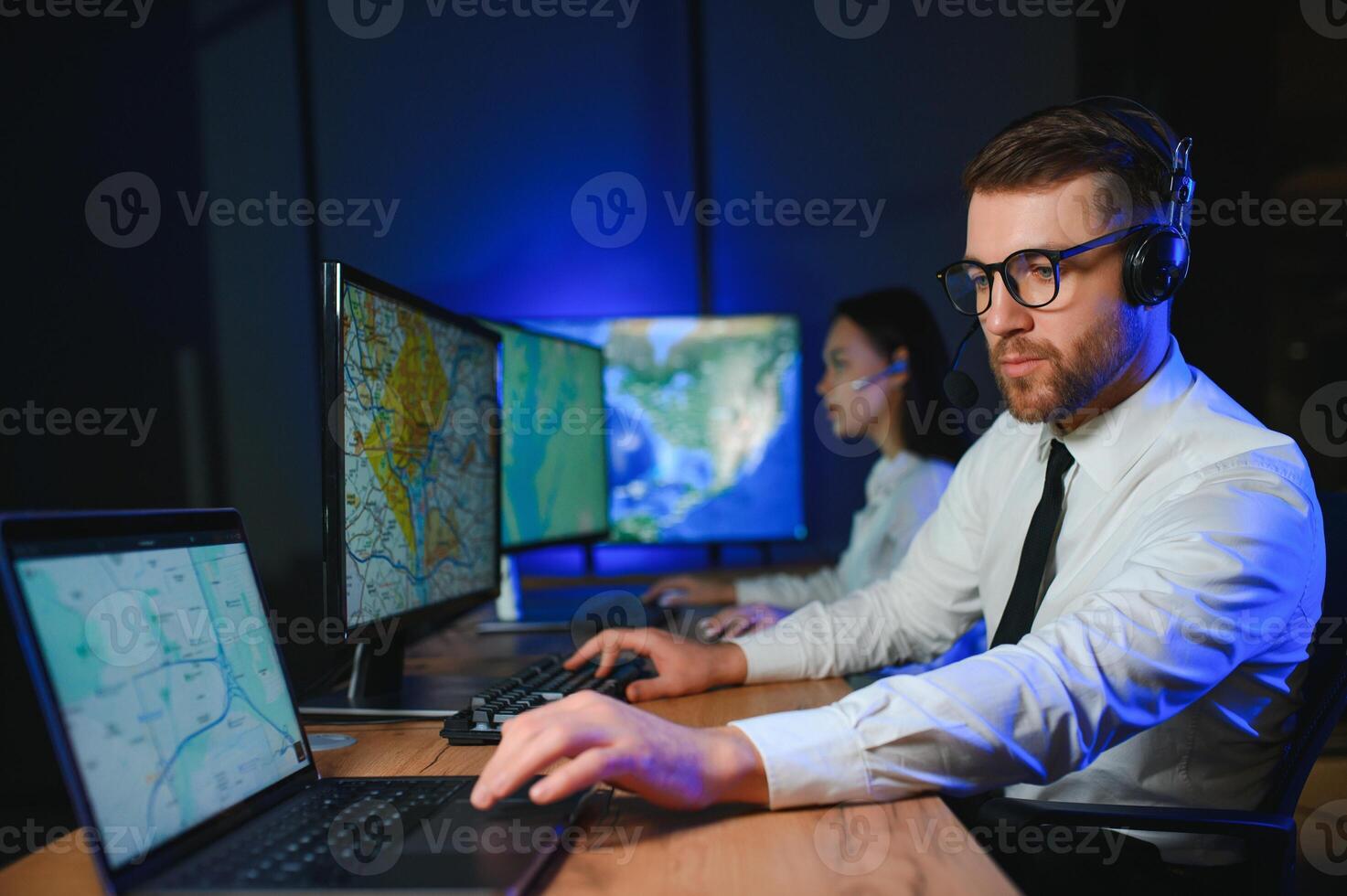 In Monitoring Room Technical Support Specialist Speaks into Headset. His Colleagues are Working in the Background photo