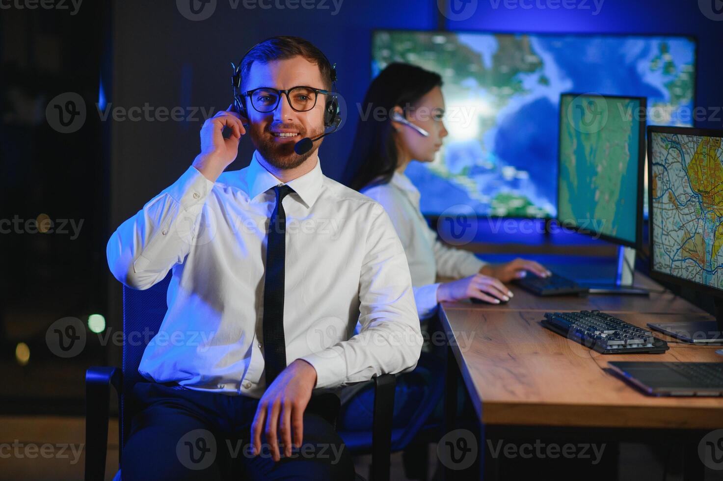 In Monitoring Room Technical Support Specialist Speaks into Headset. His Colleagues are Working in the Background photo