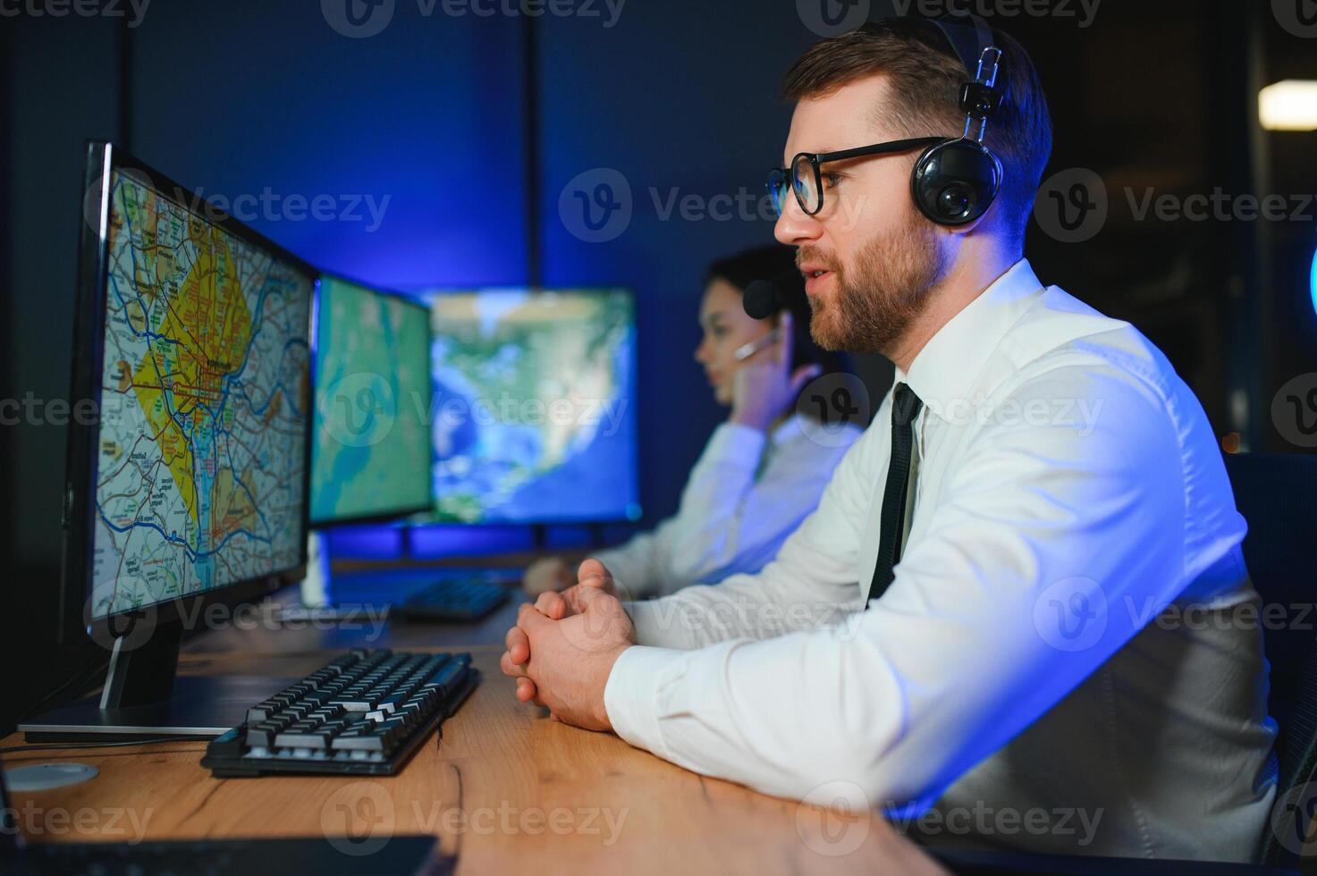 In Monitoring Room Technical Support Specialist Speaks into Headset. His Colleagues are Working in the Background photo