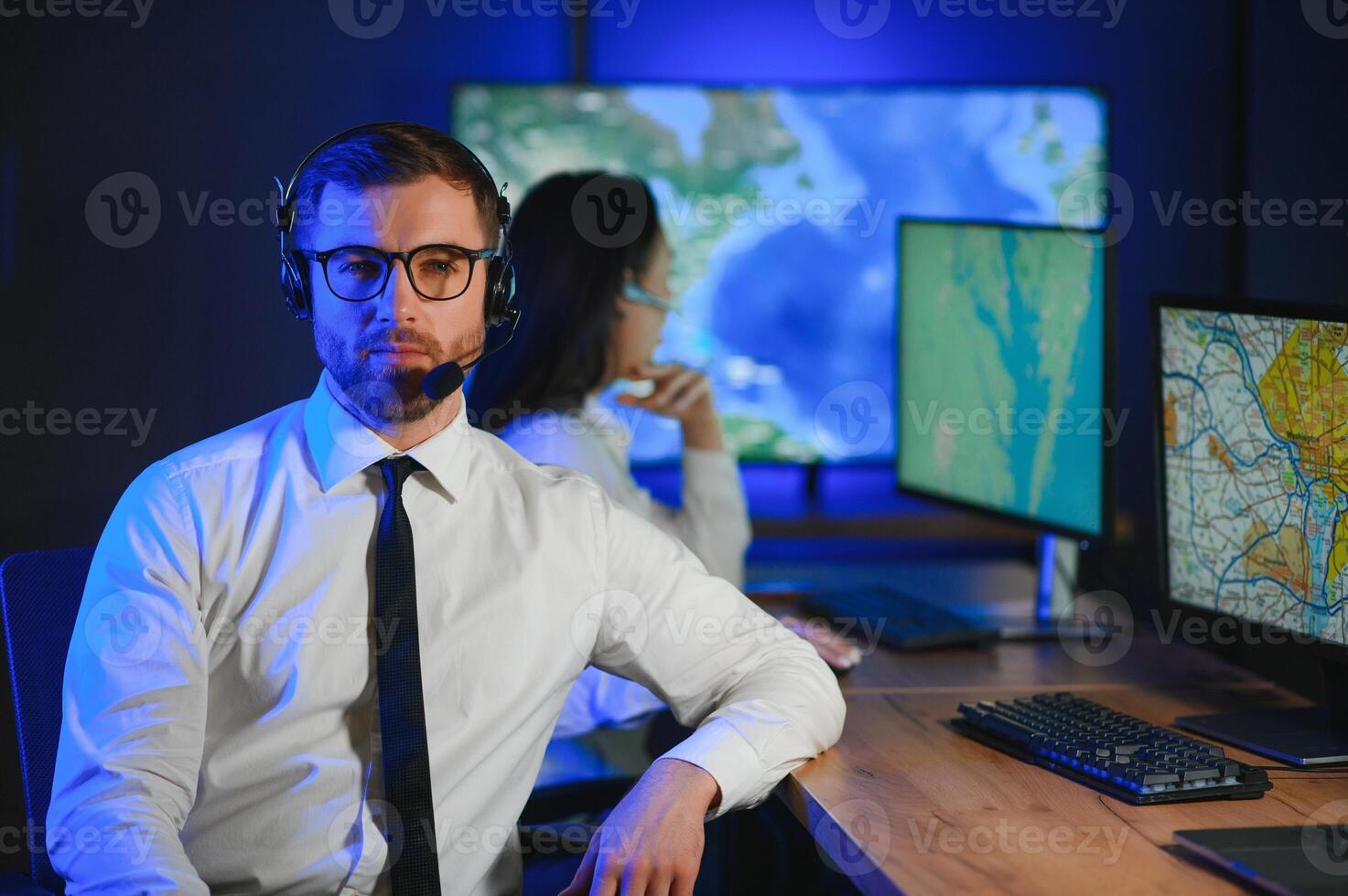 In Monitoring Room Technical Support Specialist Speaks into Headset. His Colleagues are Working in the Background photo