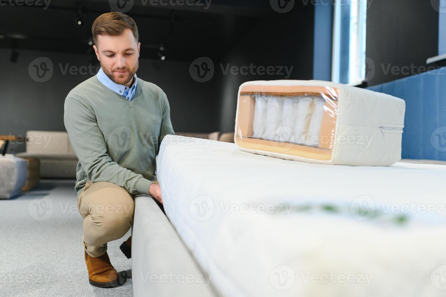 Young male customer examining orthopedic mattress on sale at furniture store, copy space photo