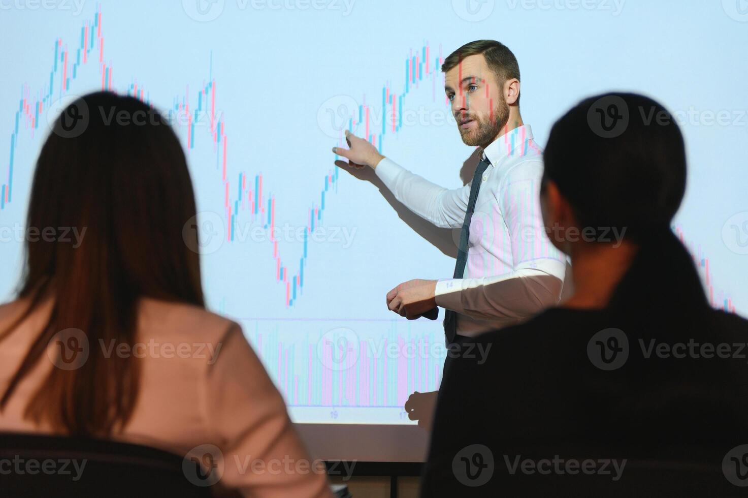 Man is standing near projector and showing graphs and business graphs. photo