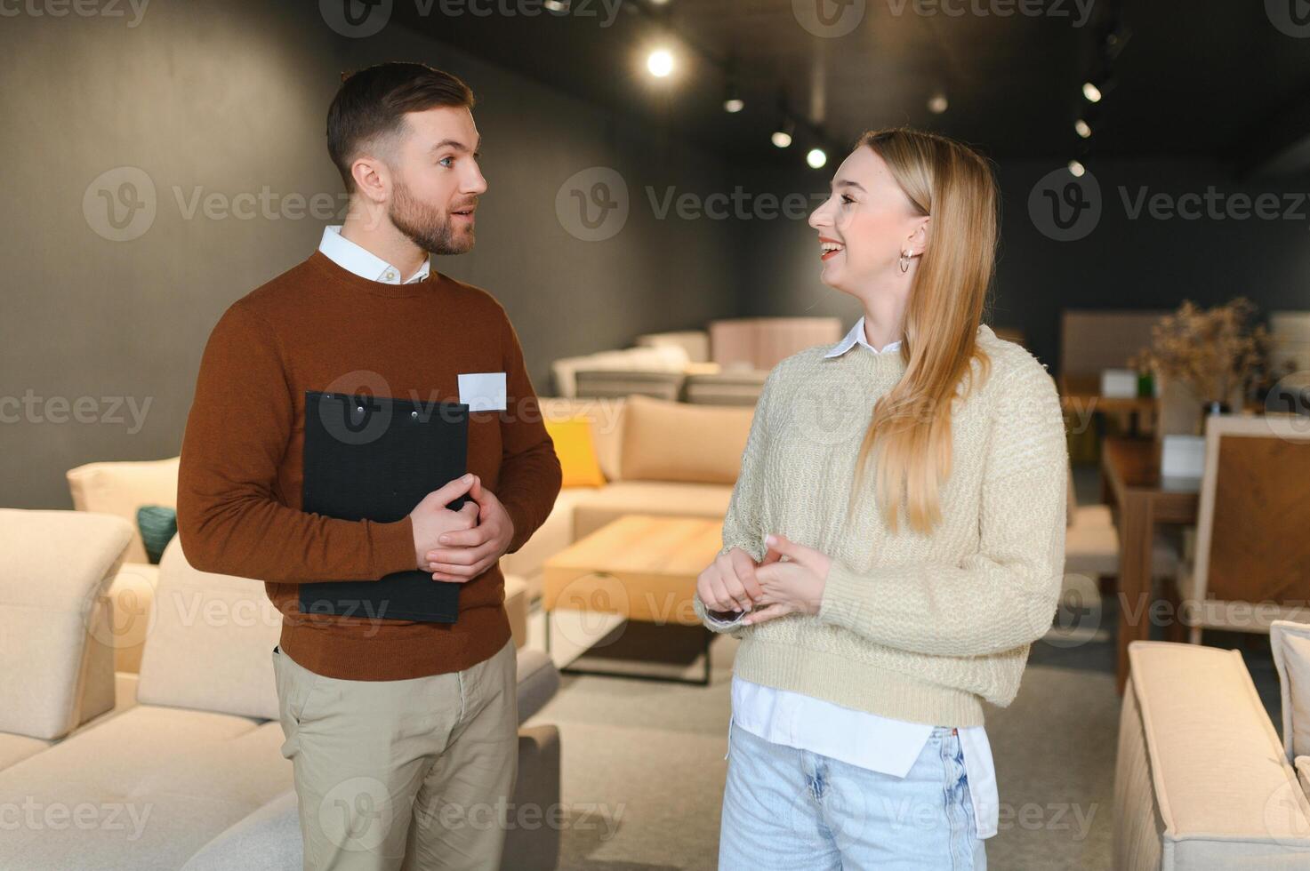 Smiling female customer looking while listening to employee discussing about sofa at store photo