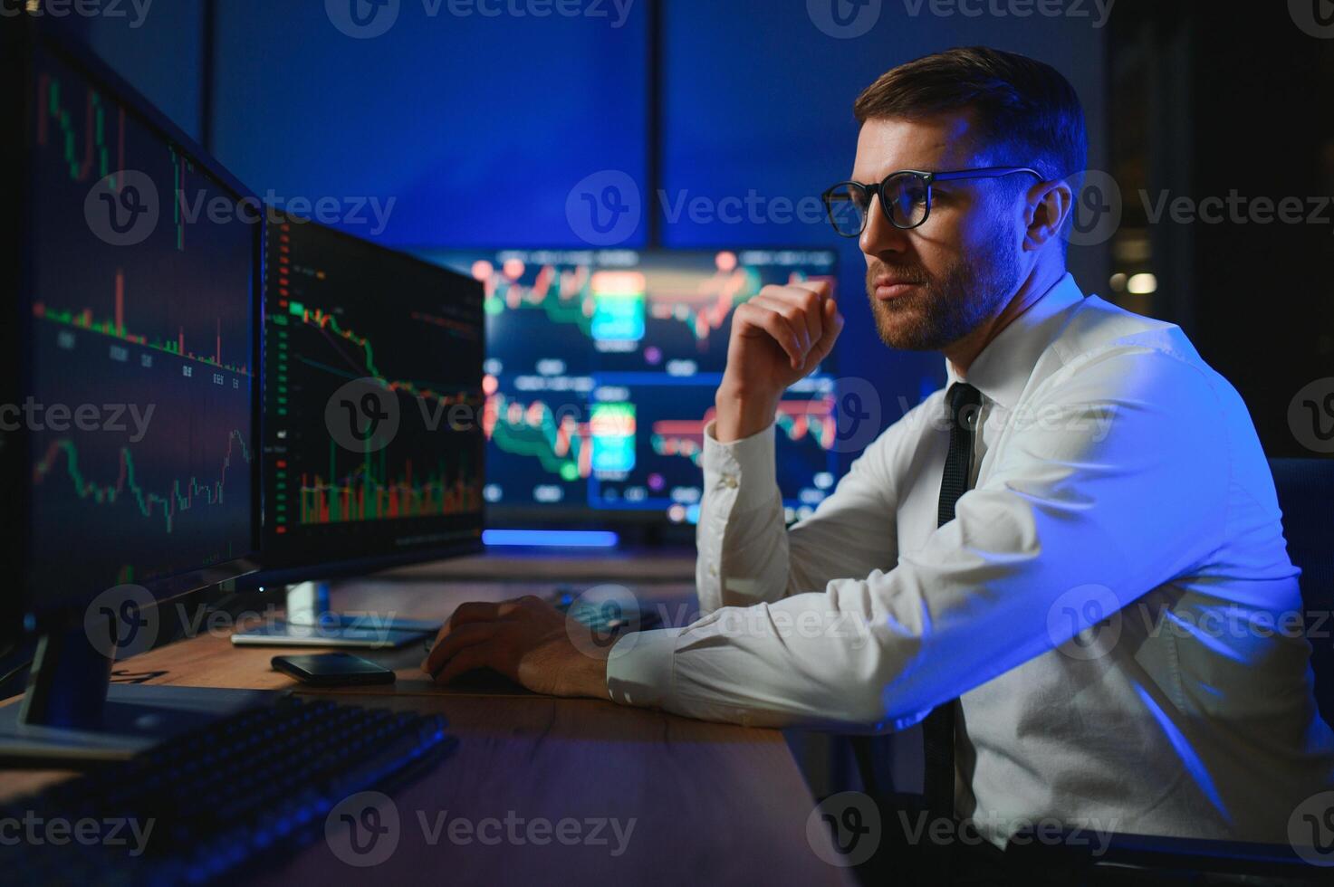 Side view of crypto broker sitting at office table, analyzing market, looking at screen photo