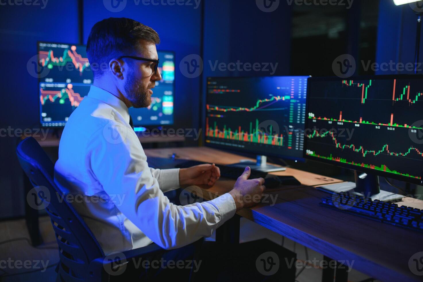 Side view of crypto broker sitting at office table, analyzing market, looking at screen photo