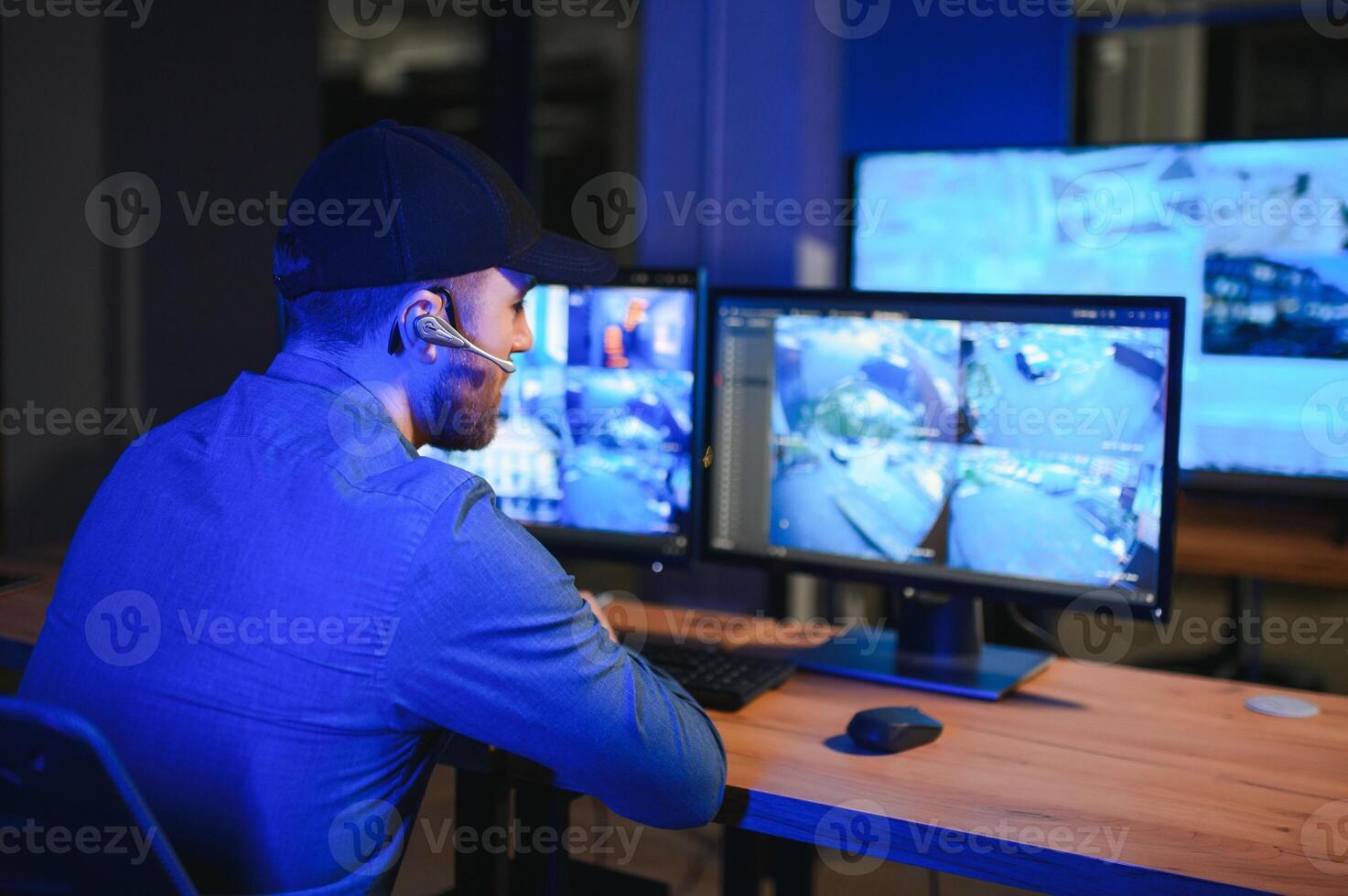 Rear view of security system operator looking at CCTV footage at desk in office photo