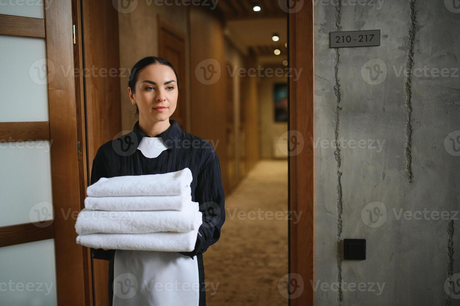 The maid is standing in the corridor of the hotel and holding clean towels photo
